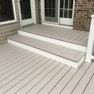 A light gray composite deck with two steps leading up to glass sliding doors on a brick and siding house exterior.