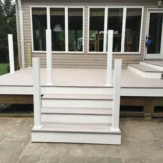 A set of light-colored steps with white posts leads up to a deck attached to a house with large windows.