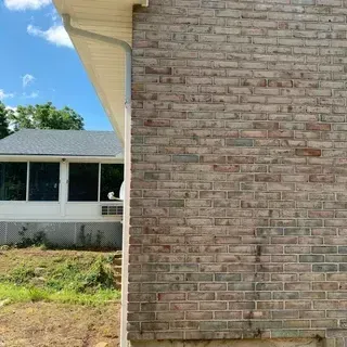A close-up of a tan brick wall corner with a white, enclosed sunroom visible in the background against a blue sky.