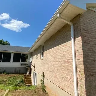 The side exterior of a brick house featuring a white gutter system and downspout, with a small staircase leading to a porch.