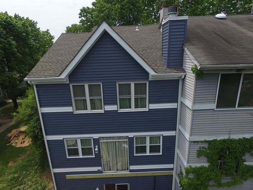 A three-story dark blue building exterior with white trim, gray shingled roof, and a chimney, viewed from above.