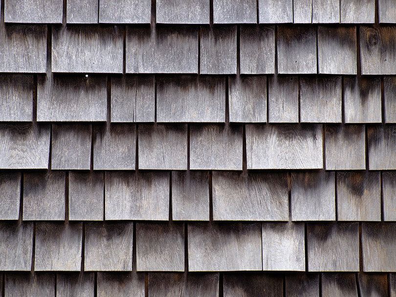 Close-up of weathered gray wooden shingles or shakes arranged in overlapping horizontal rows.