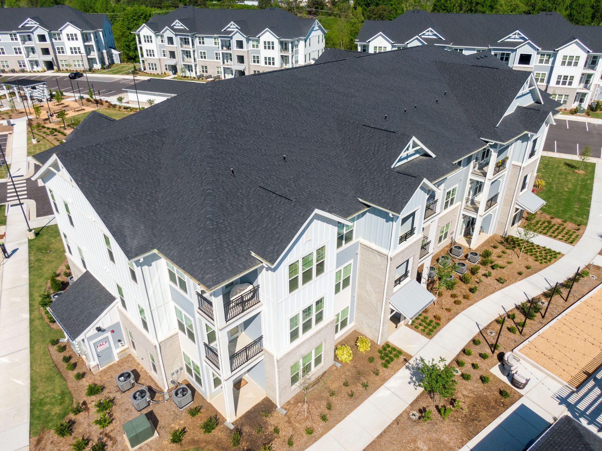 An elevated, angled view of a modern multi-story apartment complex with dark shingled roofs and white siding.