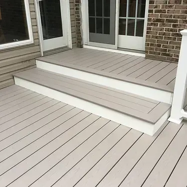 Light gray composite deck with two steps leading to a white-trimmed sliding glass door and brick exterior wall.