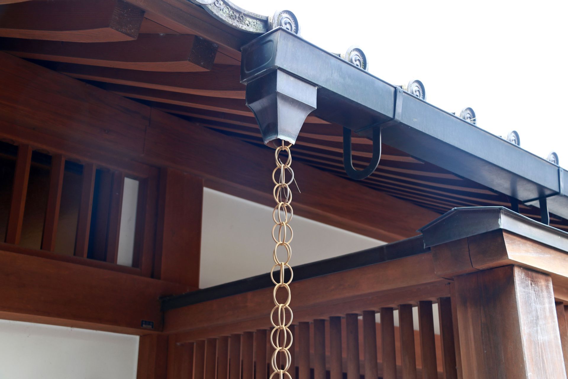 Copper rain chain hanging from a dark gutter on a wooden Japanese-style building.