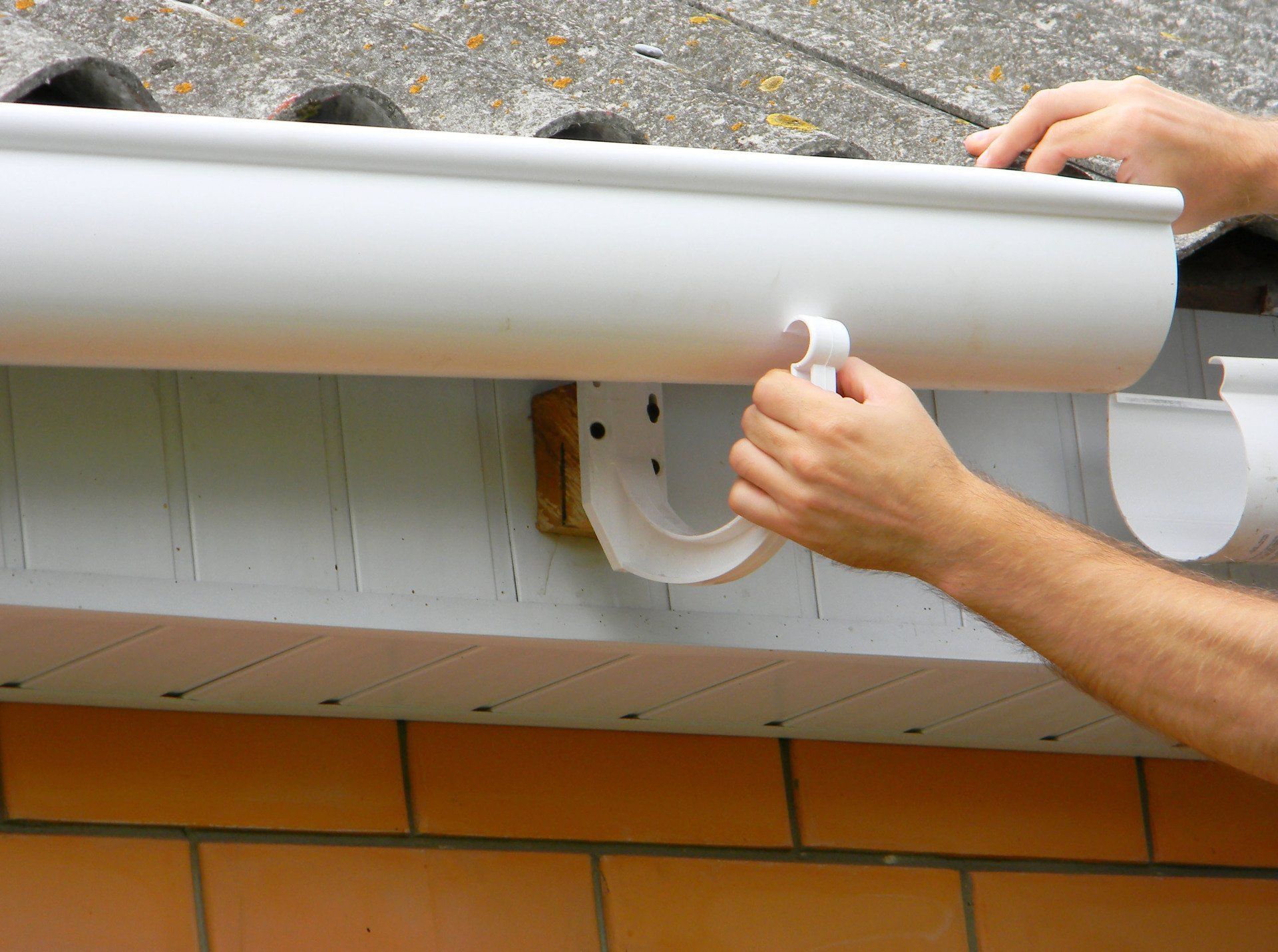 Hands installing white gutter, attaching to the downspout.