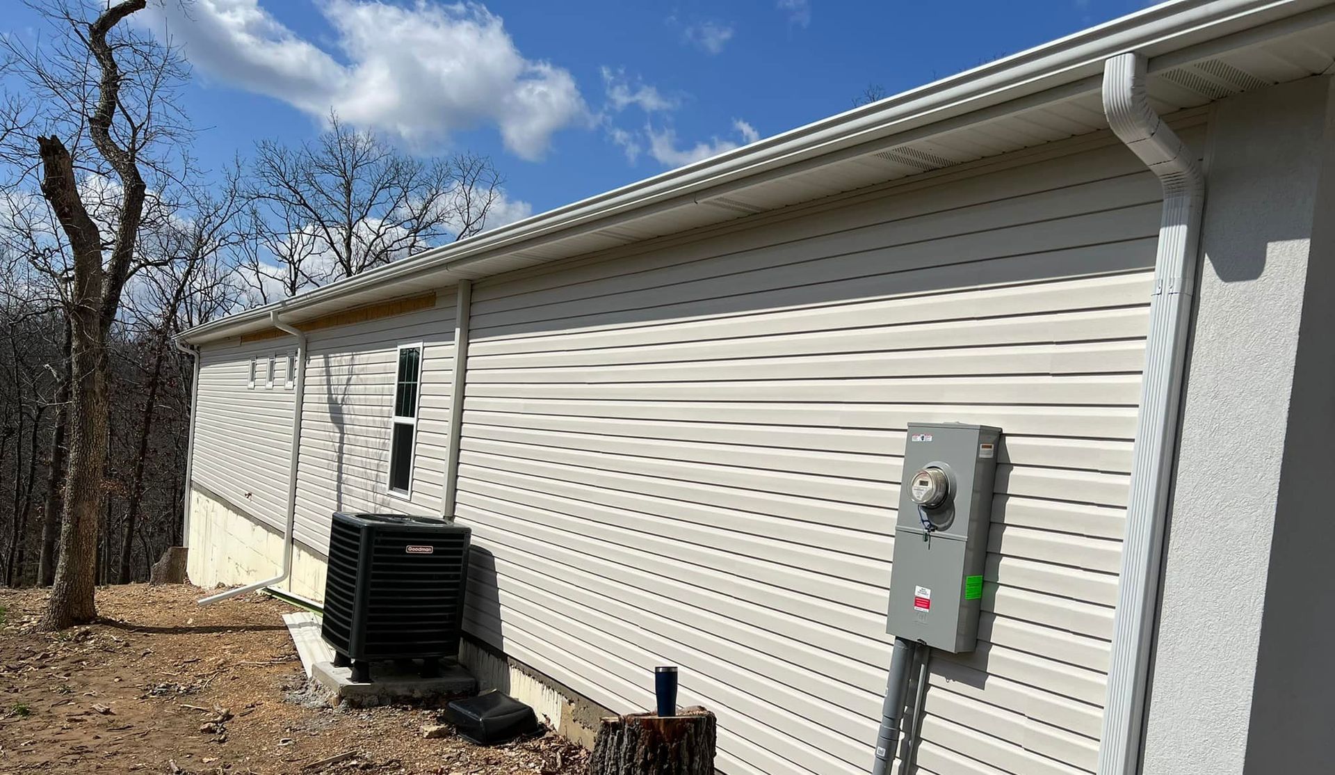 White siding on a building with an AC unit and electrical box outside against a blue sky.
