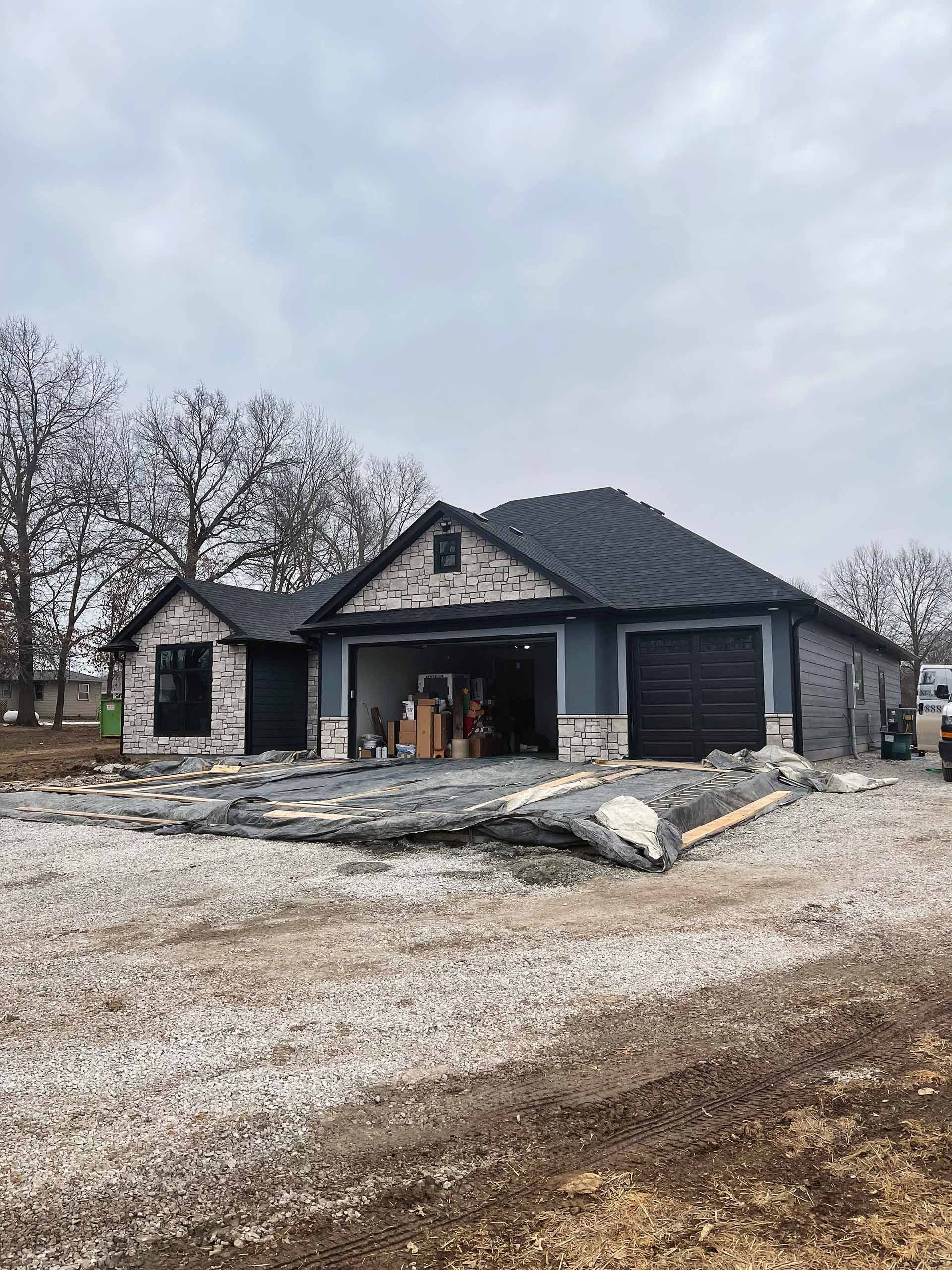 New house under construction with brick and dark siding, two-car garage. Overcast sky.