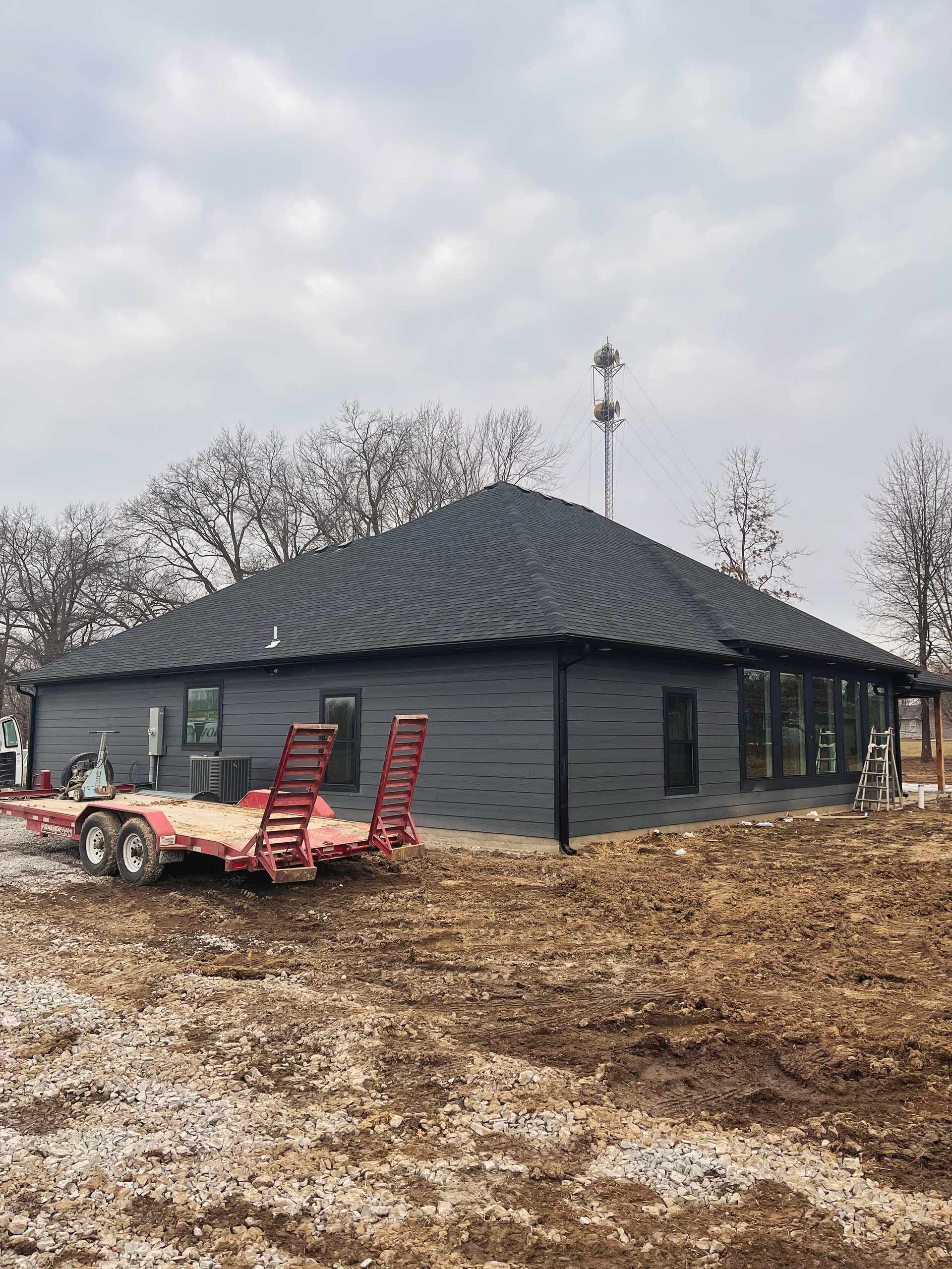 New dark-sided house with black roof, on construction site with trailer. Cloudy sky background.