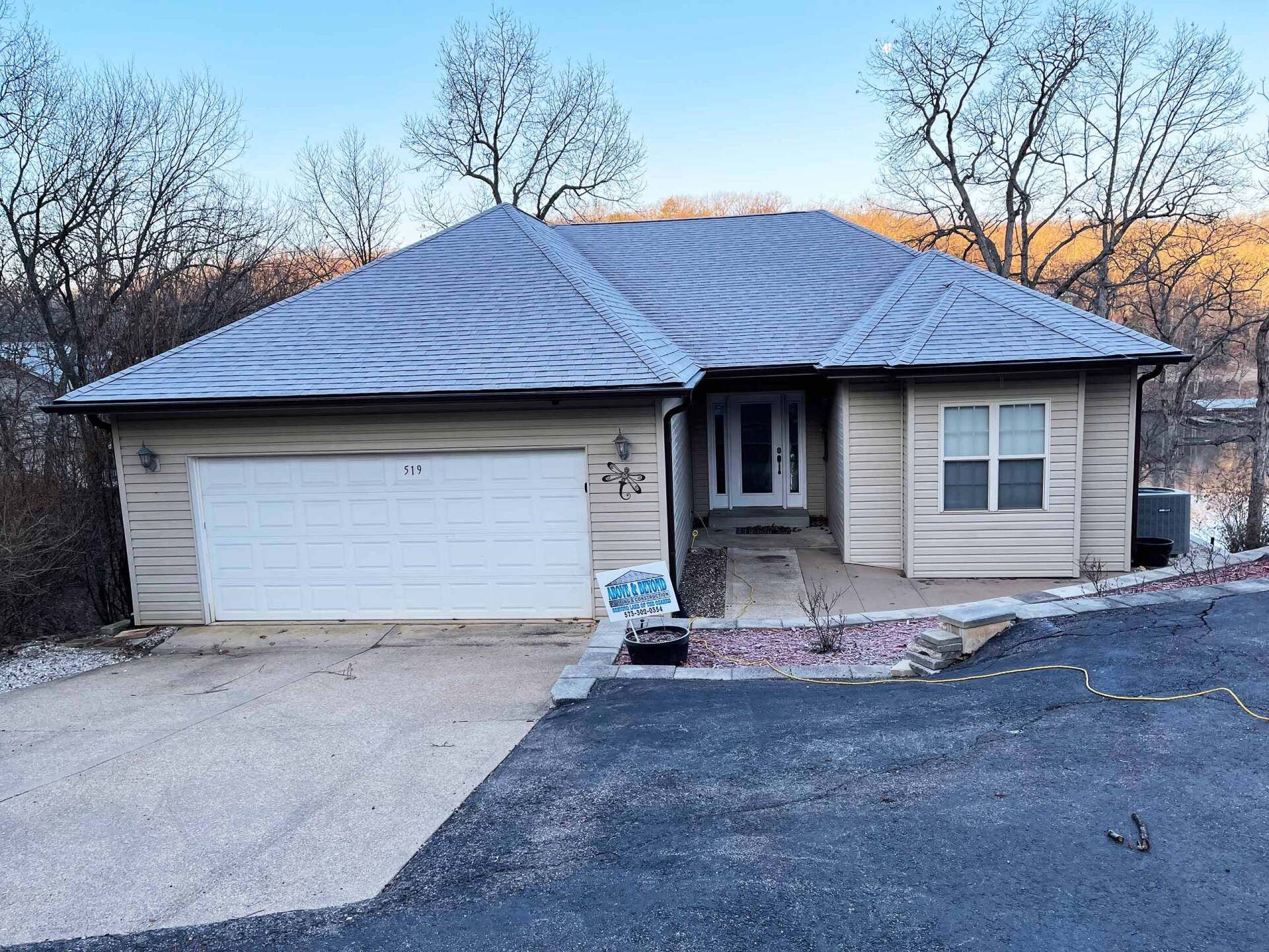 House with beige siding, white garage door, and snow-covered roof; set on a hillside.