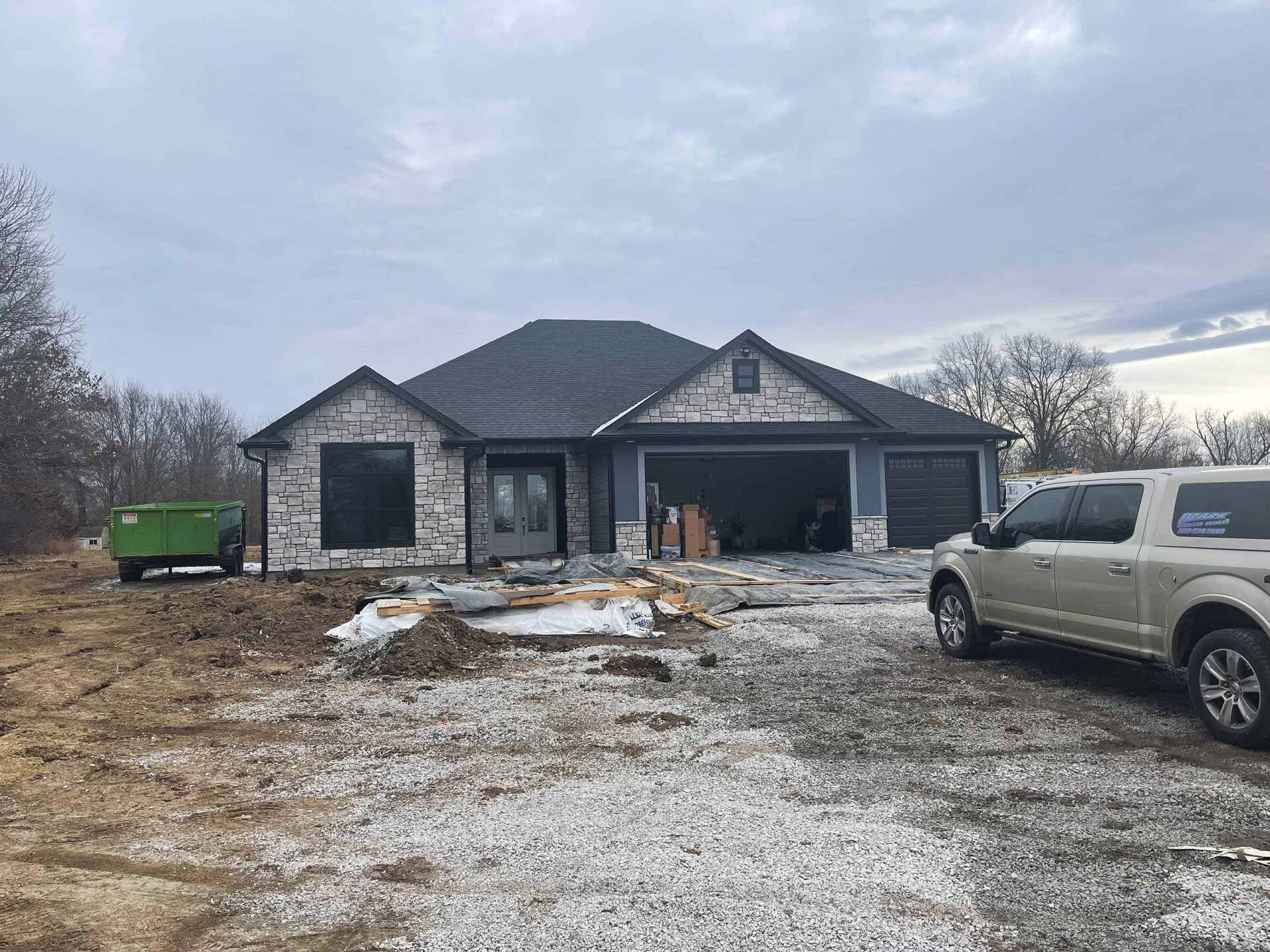 New house under construction, gray brick, blue siding, two-car garage, gravel driveway.