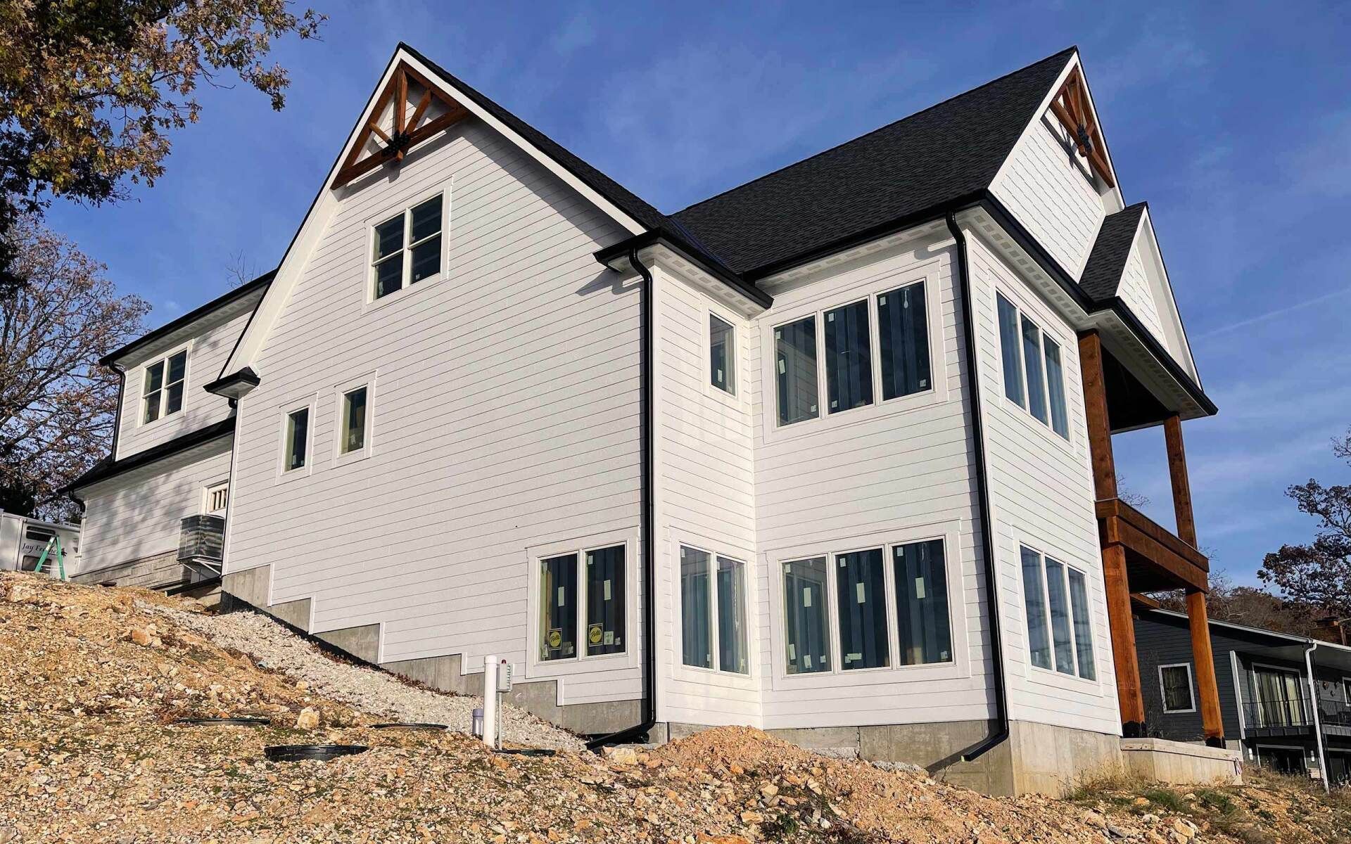 Two-story white house under construction on a hillside. Black roof, windows, and exposed wooden beams.