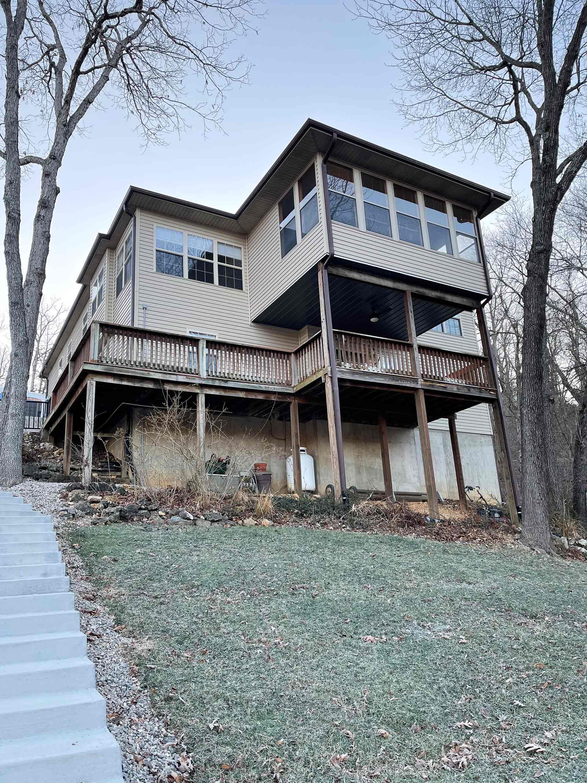 Two-story wood-sided house with decks and screened porch, set amongst bare trees and grass.