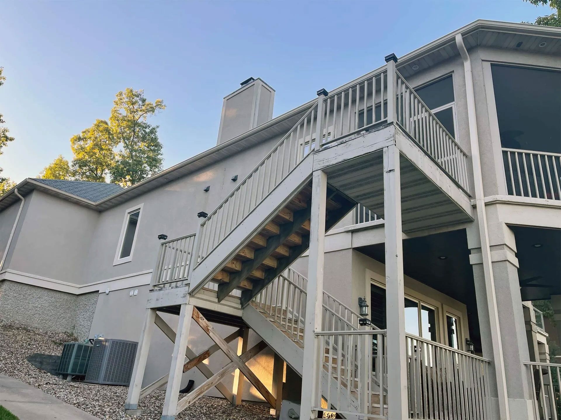 Two-story house with exterior stairs, light gray siding, and a deck.