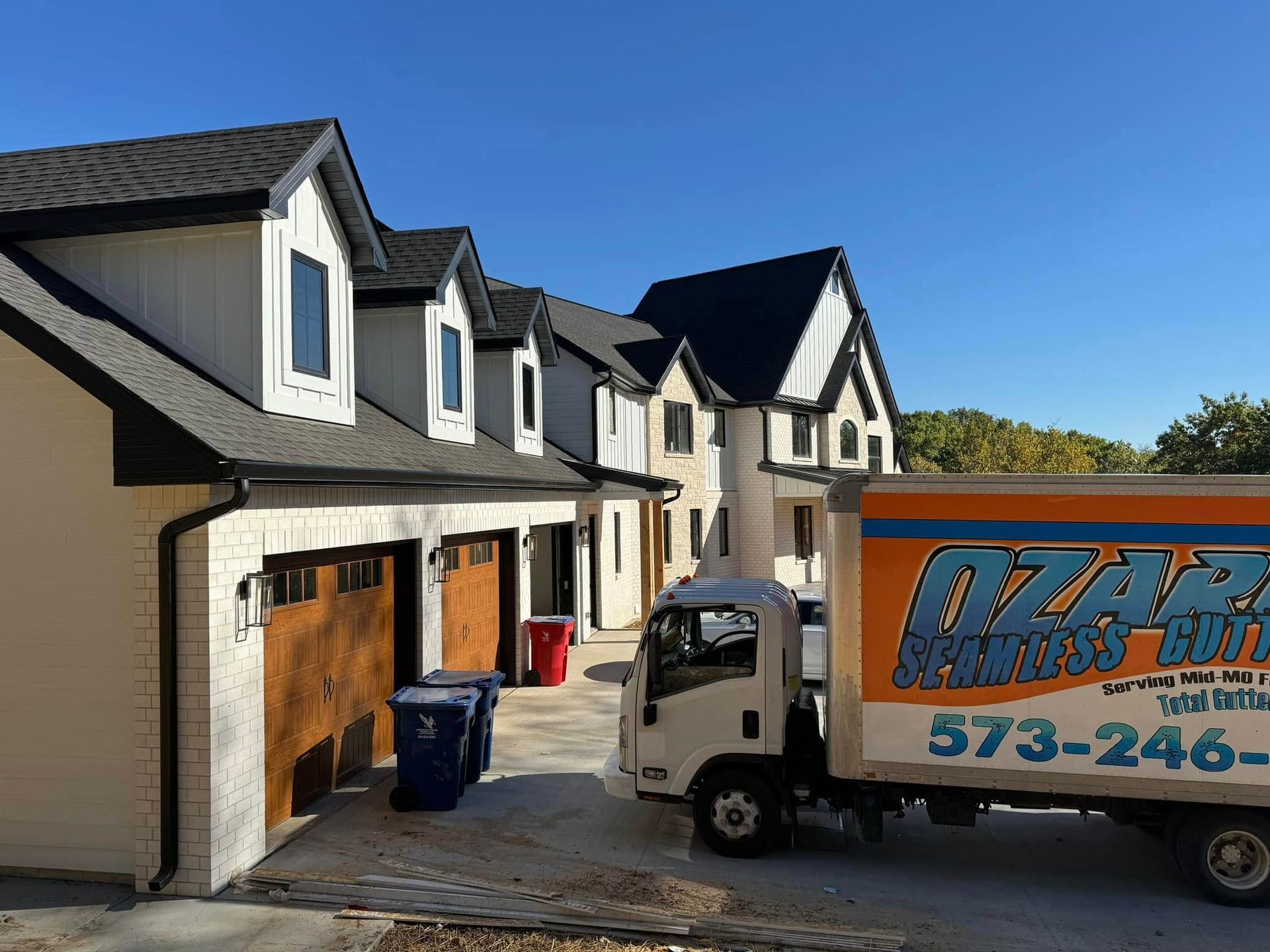 Moving truck in front of a newly built white and black house with a clear blue sky.