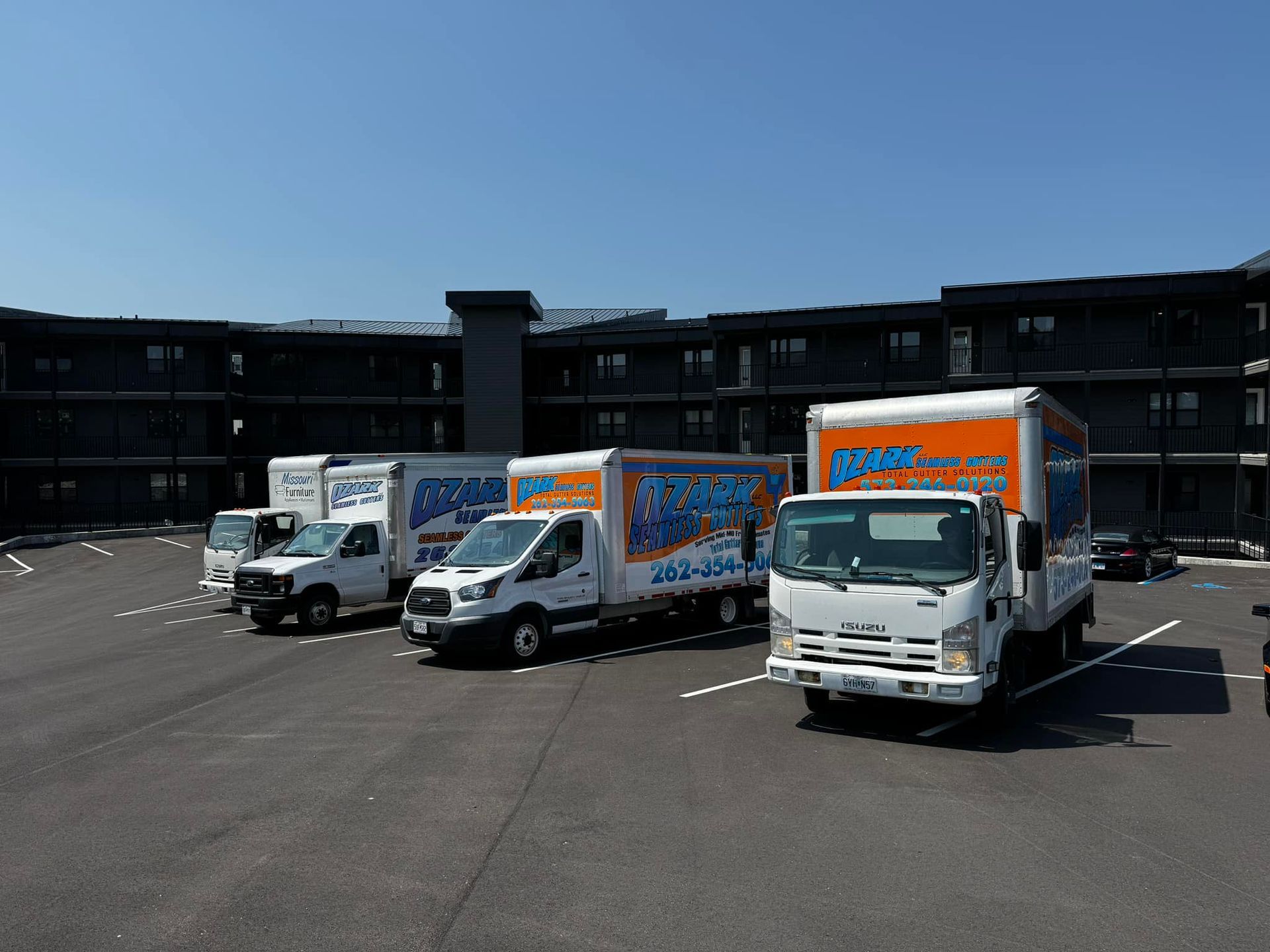 Moving trucks parked in front of a dark building on a sunny day.