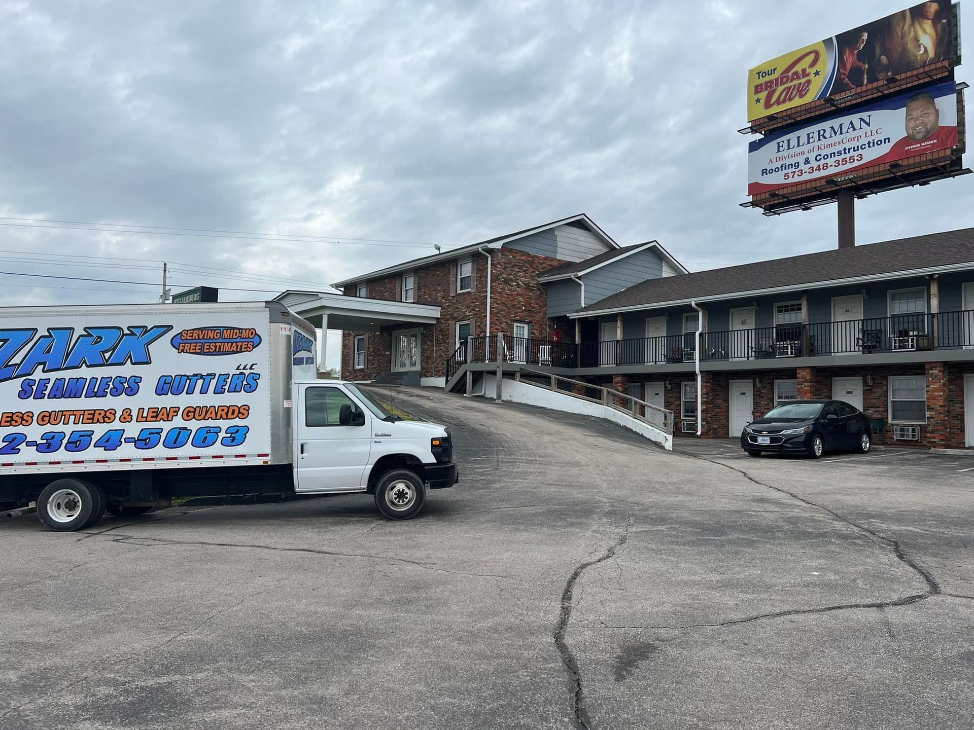 White delivery truck parked at a motel with a billboard; overcast sky.