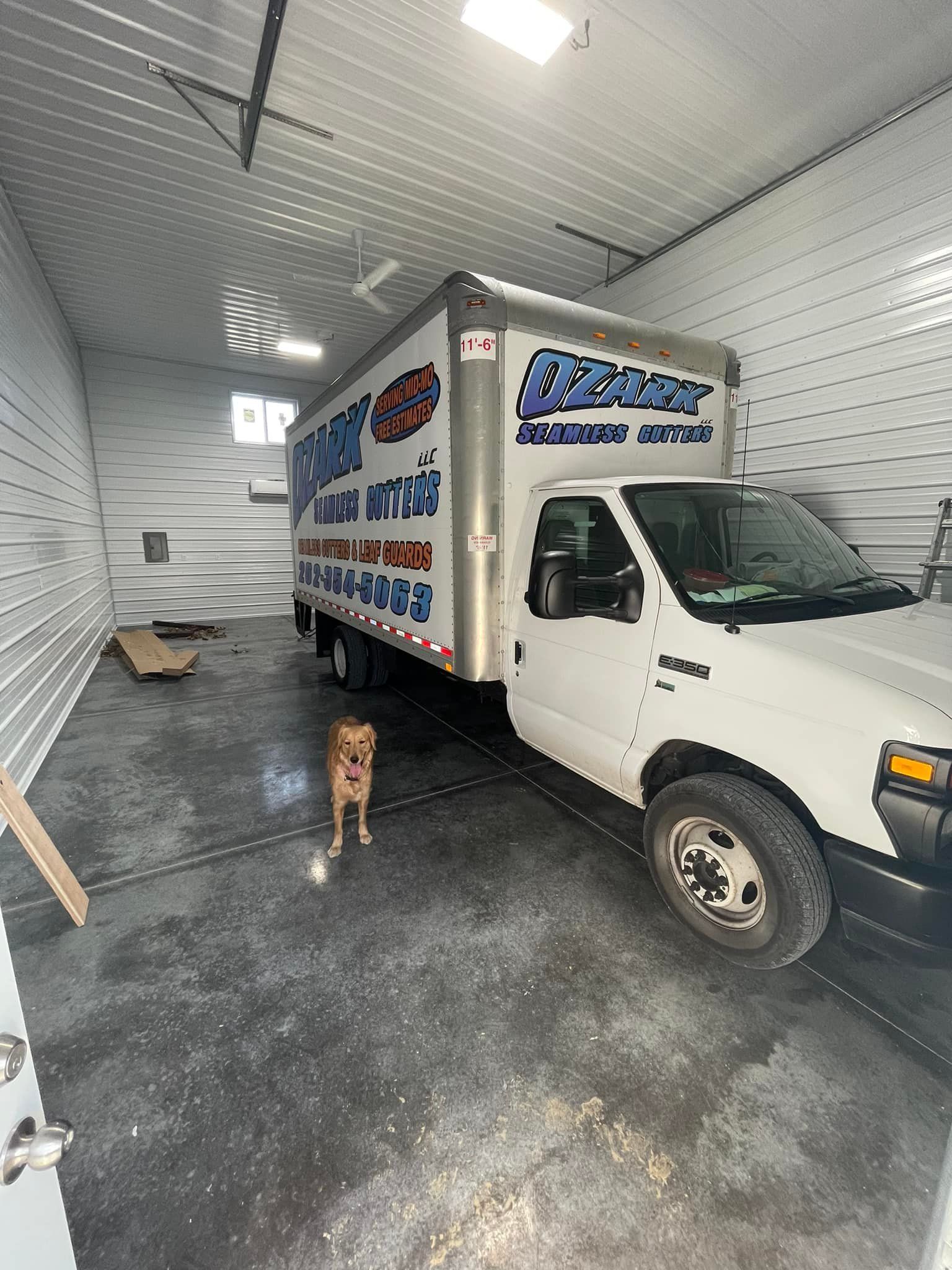 White moving truck inside a garage with a dog standing near it.