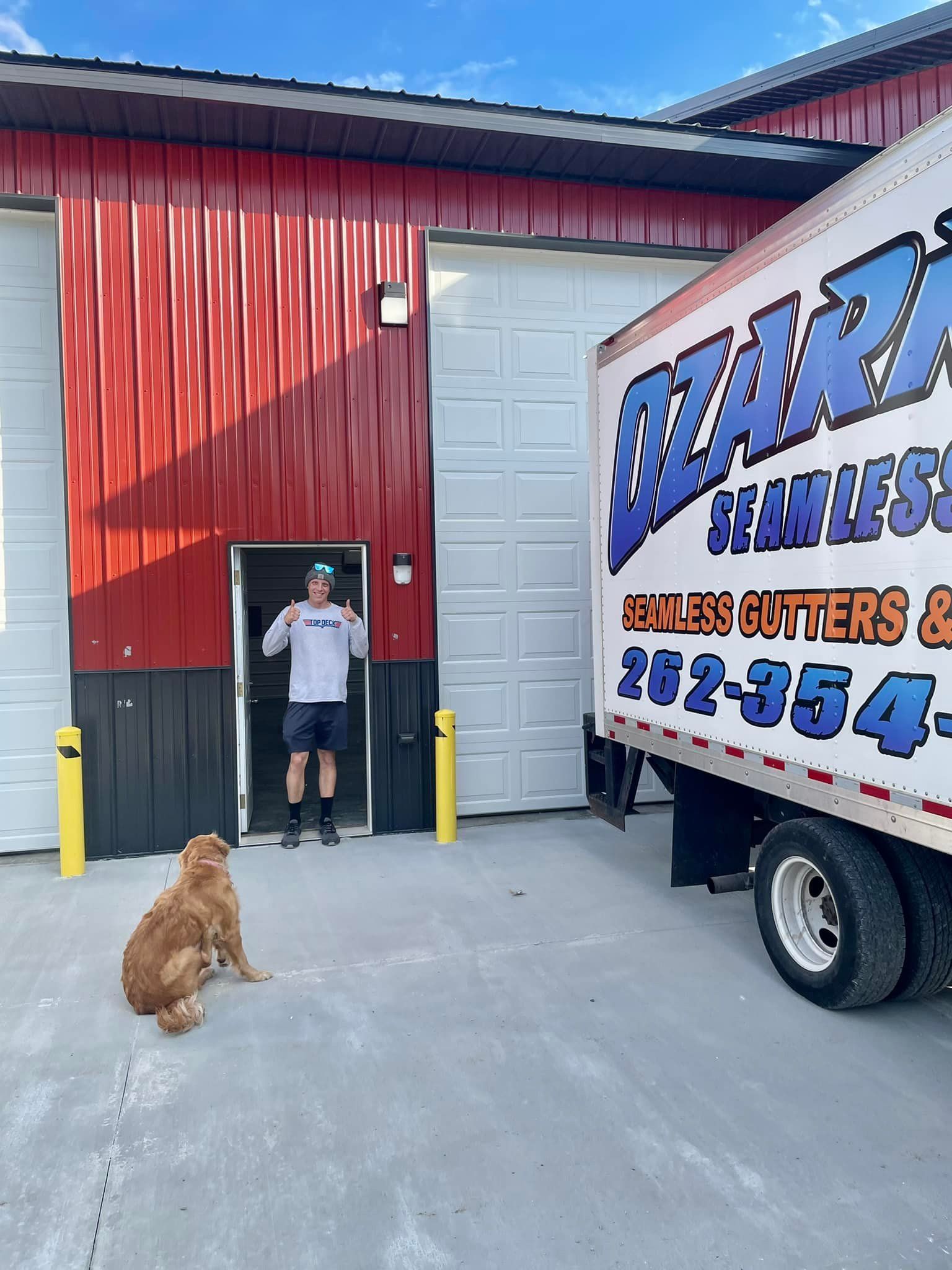 A man stands in a doorway next to a truck. A dog sits on the ground.