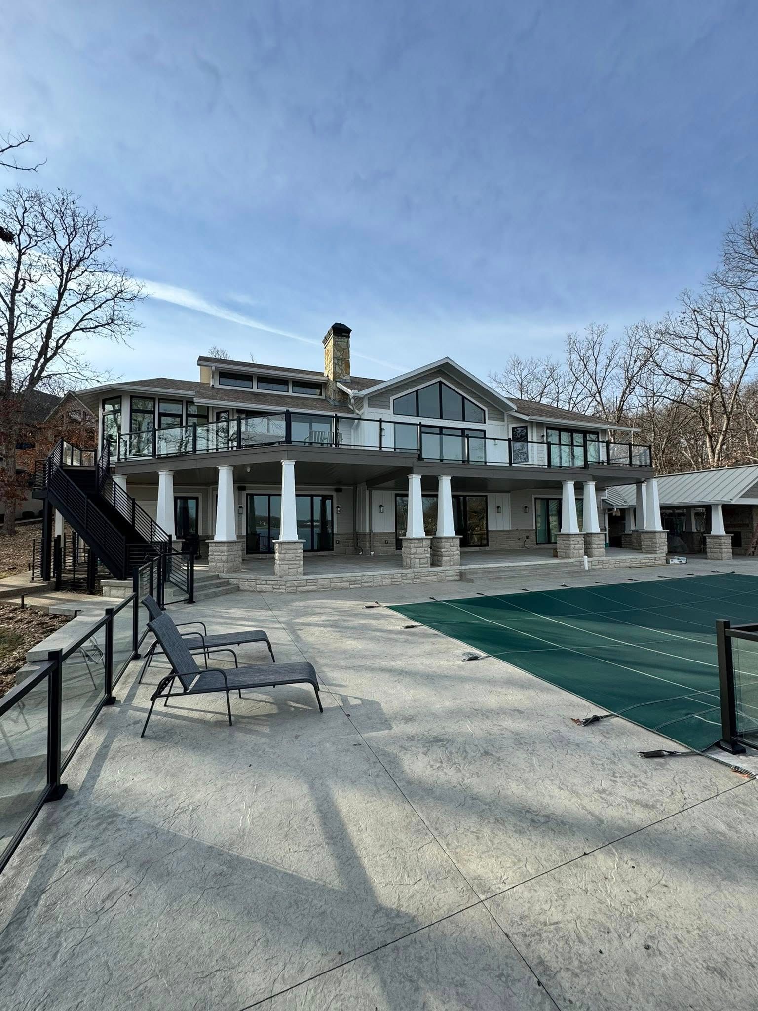 Large house with a pool and deck overlooking a body of water under a blue sky.