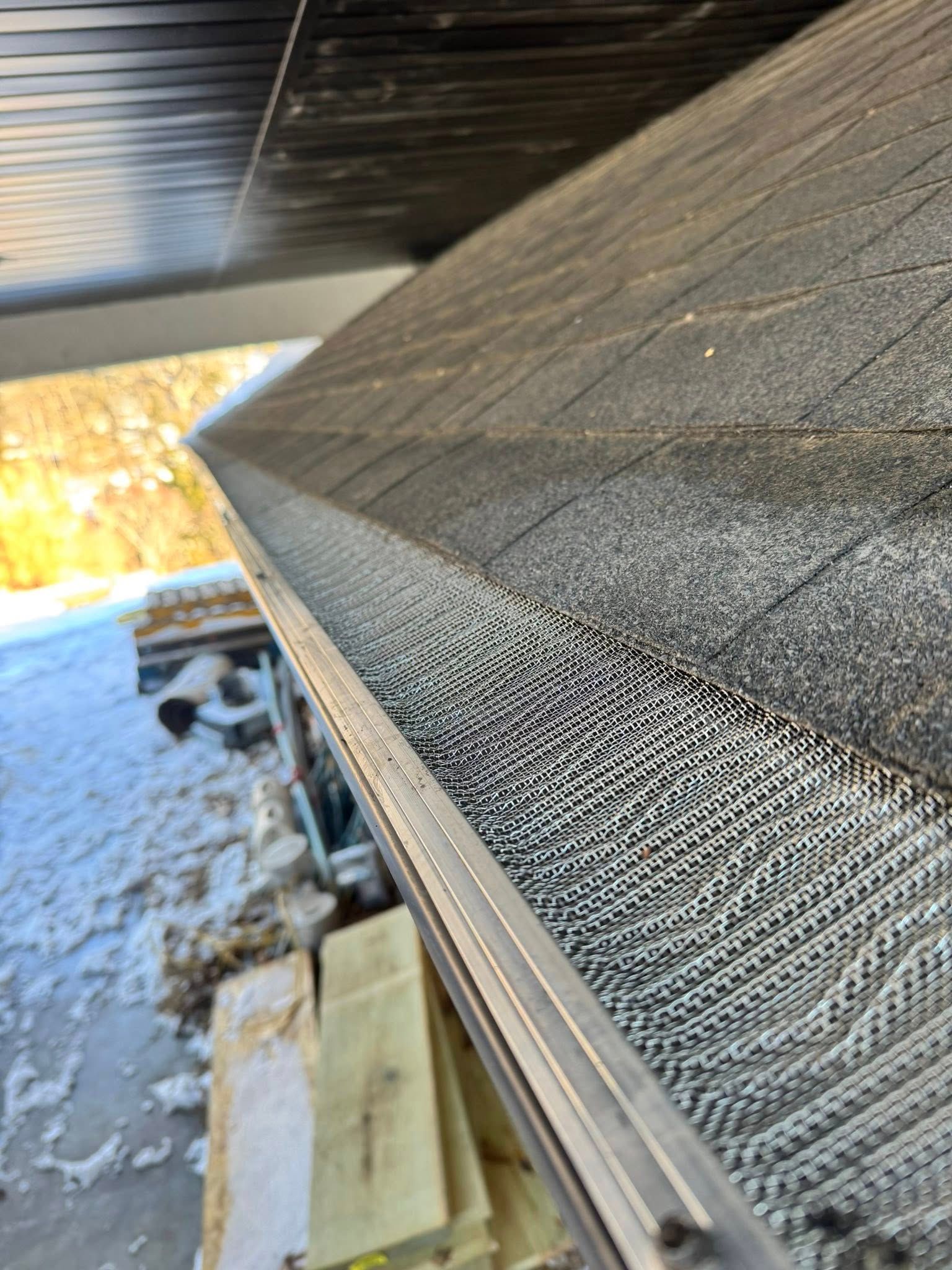 Close-up view of a gutter with mesh covering, mounted on the edge of a roof with snow nearby.