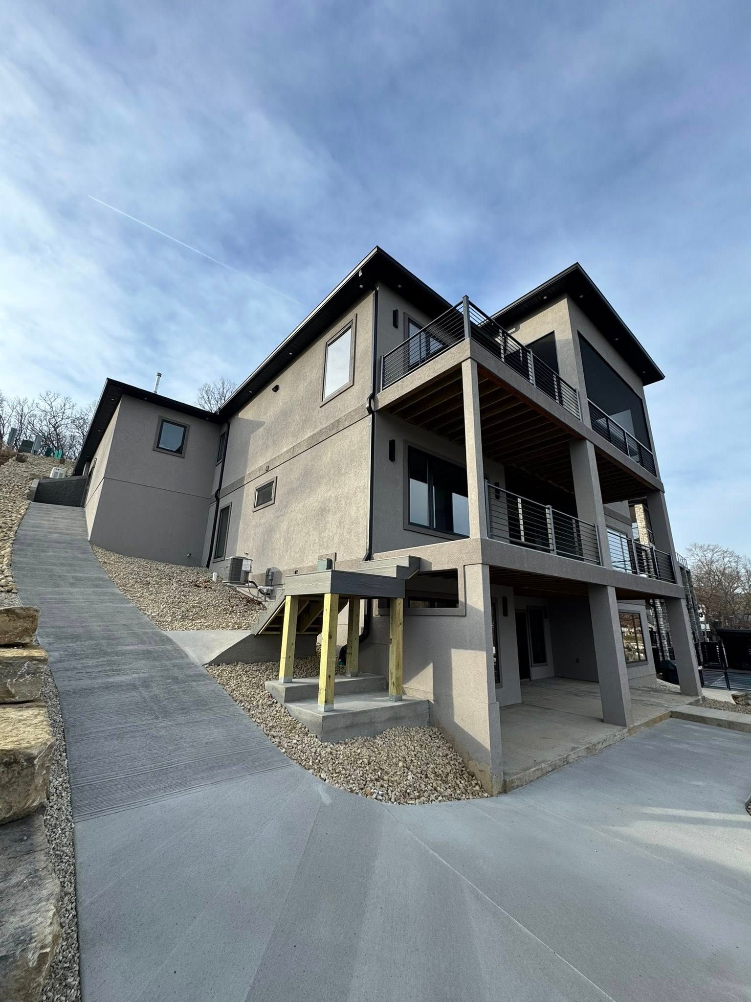 Modern two-story house with gray stucco, balconies, and a concrete driveway and walkway.