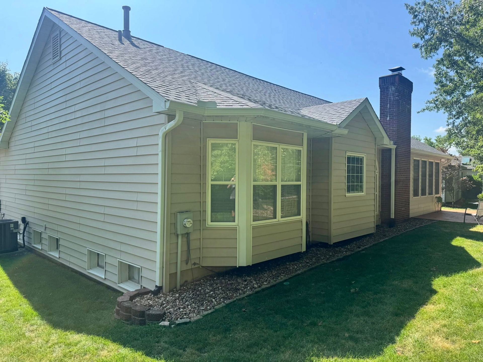 Tan house with a bay window, chimney, and a grassy yard under a blue sky.