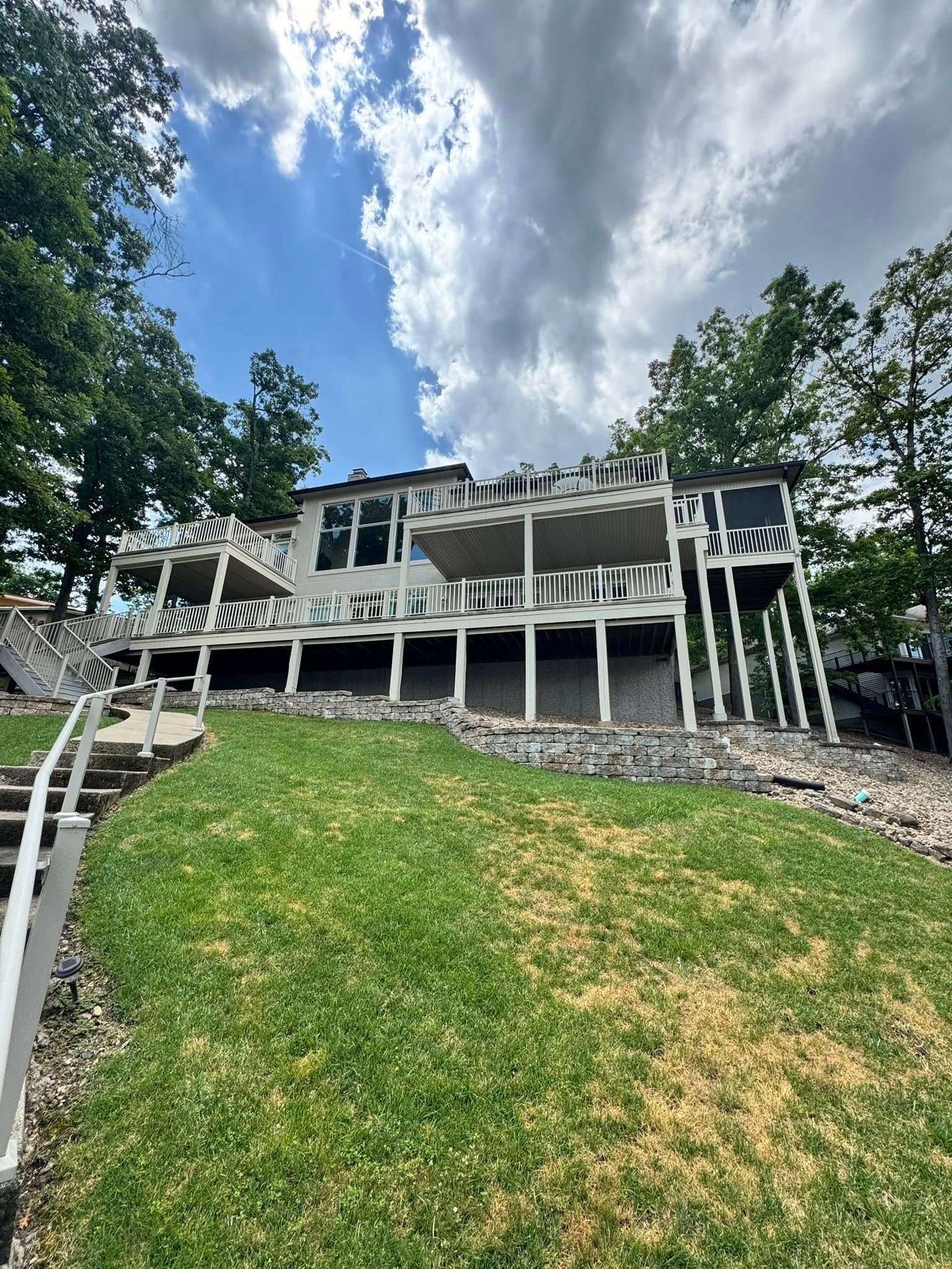 House on a hillside with a lawn and stairs leading down to a waterfront. Overcast sky.
