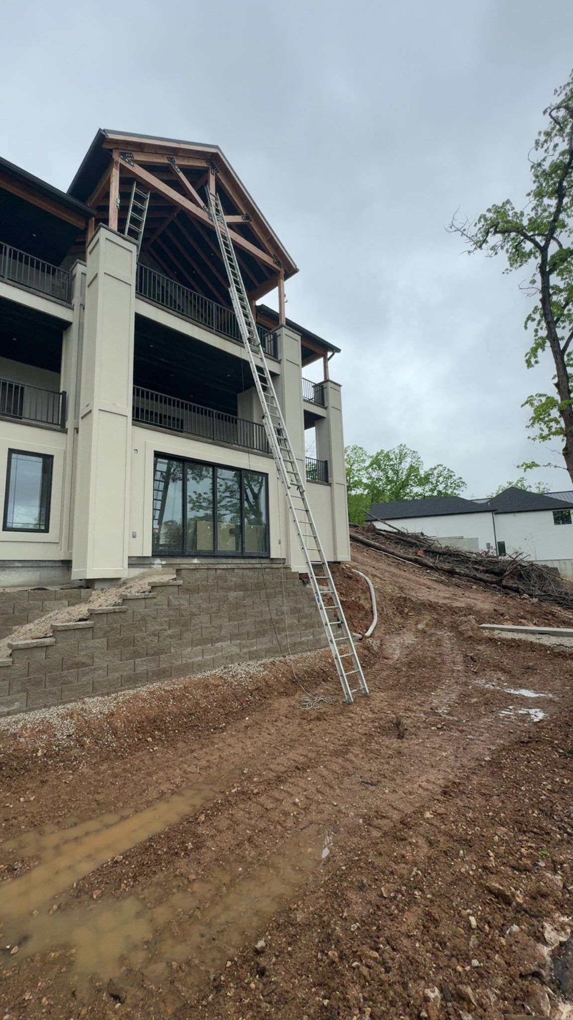 Ladder leaning against a building with exposed roof construction; construction site with dirt and cloudy sky.