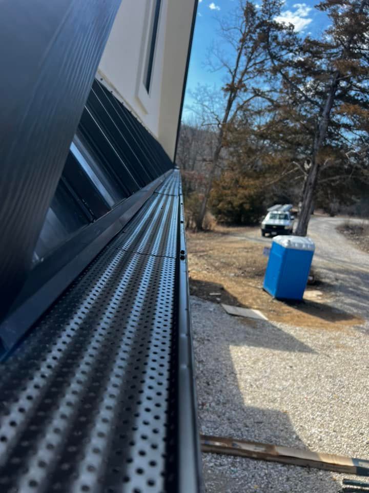 Black gutter with mesh cover installed on a house, a blue portable toilet and a vehicle are in the background.