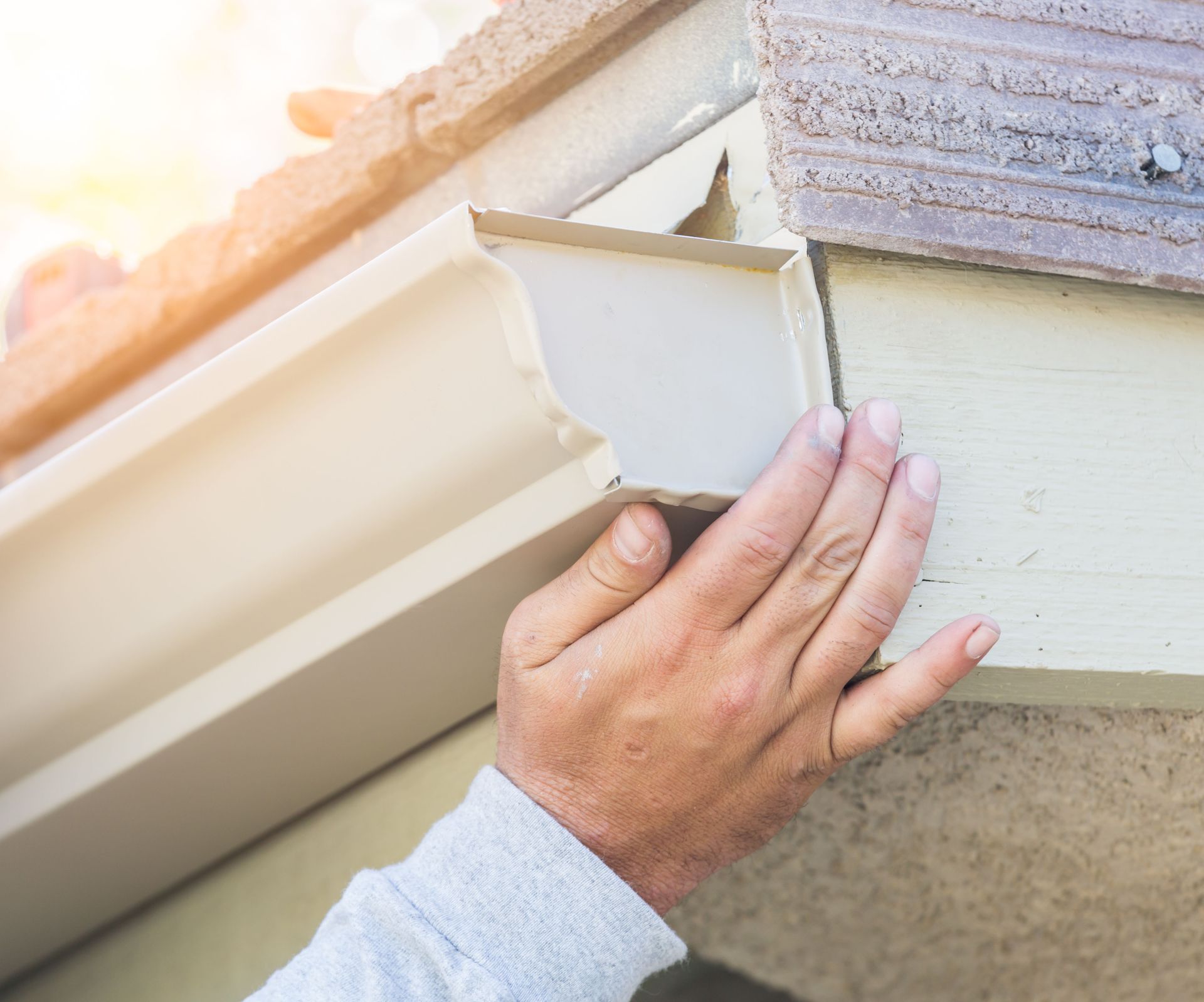 Hand installing beige gutter on a building's exterior.