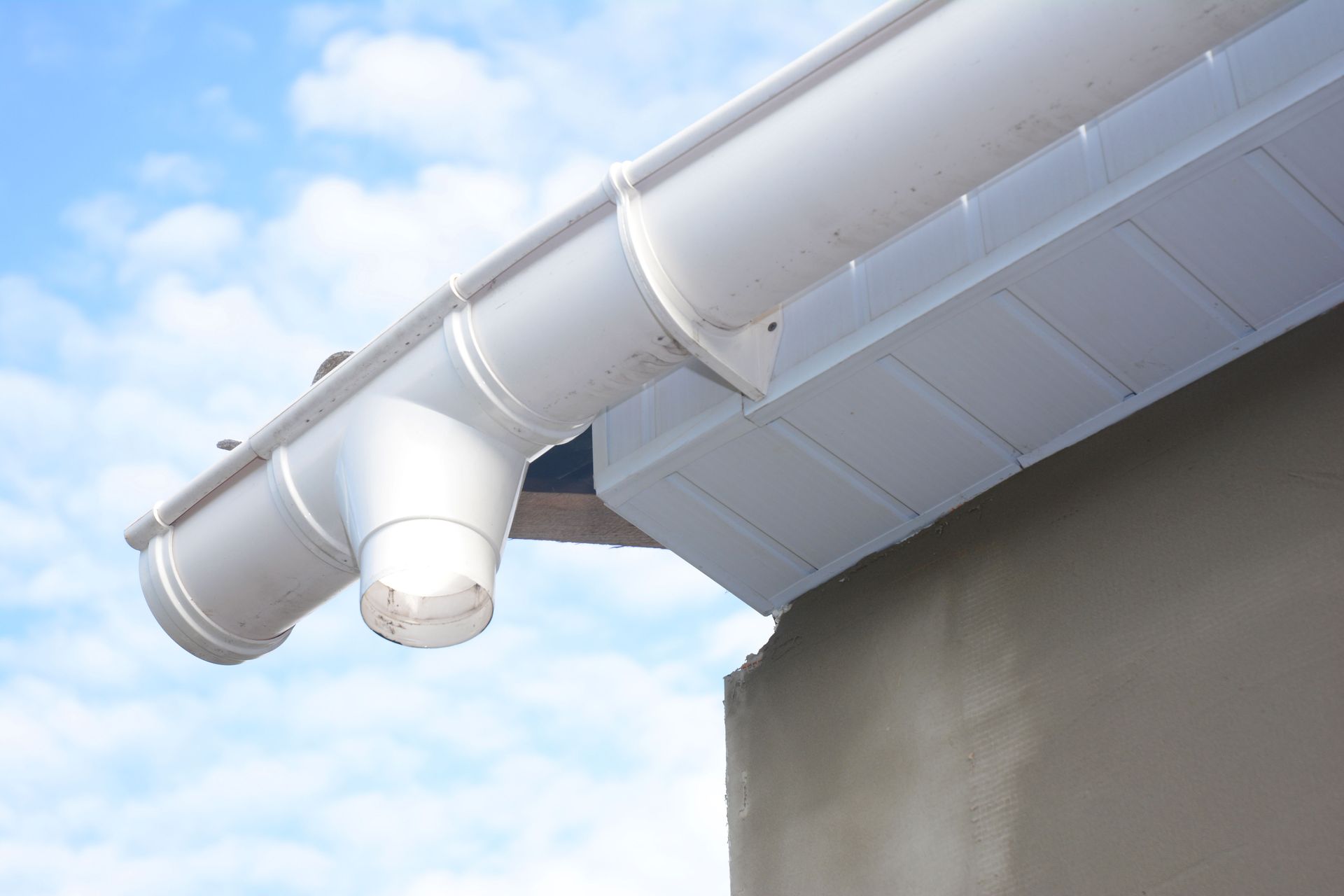 White rain gutter system on a building, angled against a blue sky.