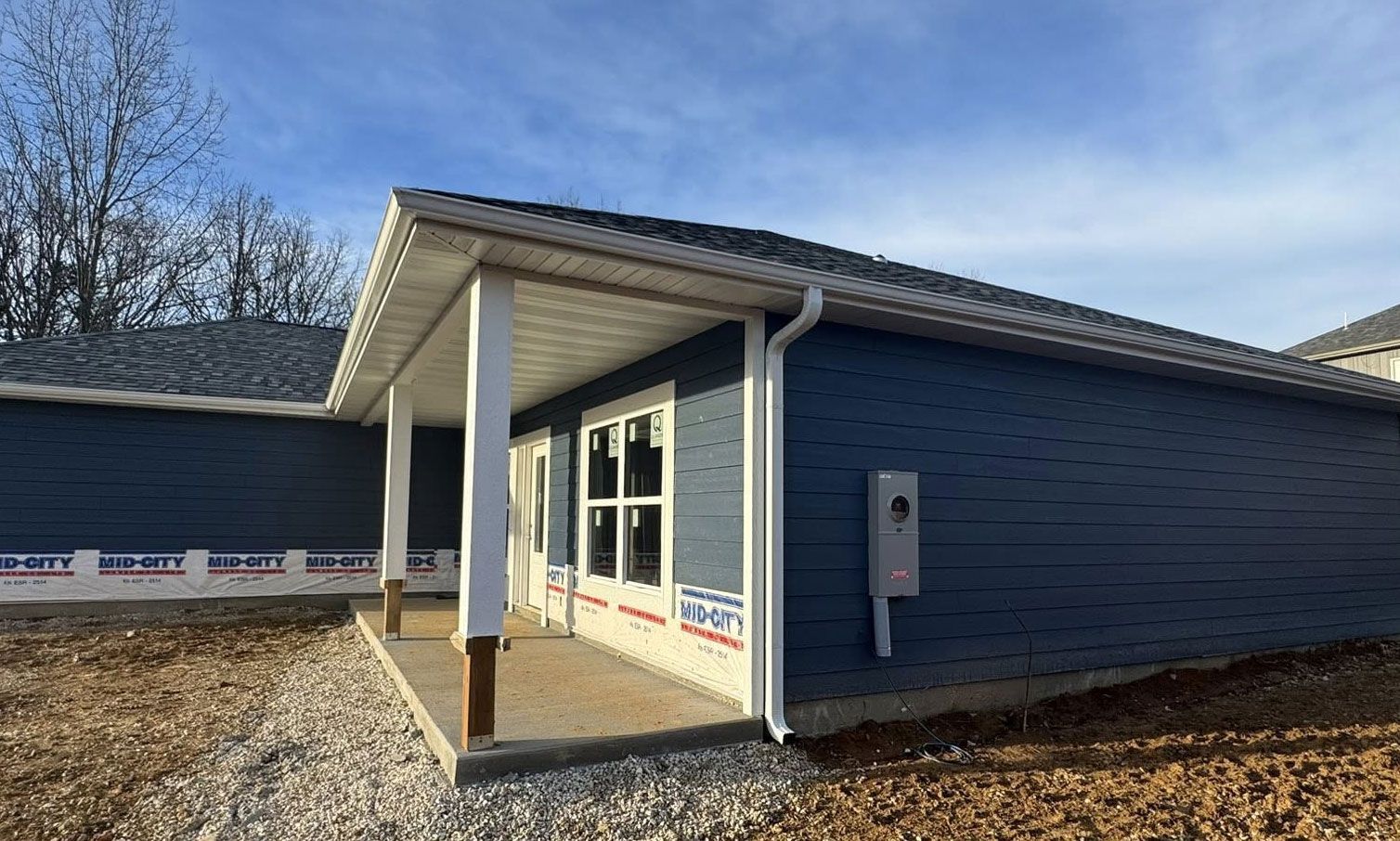 Blue-sided house with a porch and white trim under construction on a sunny day.