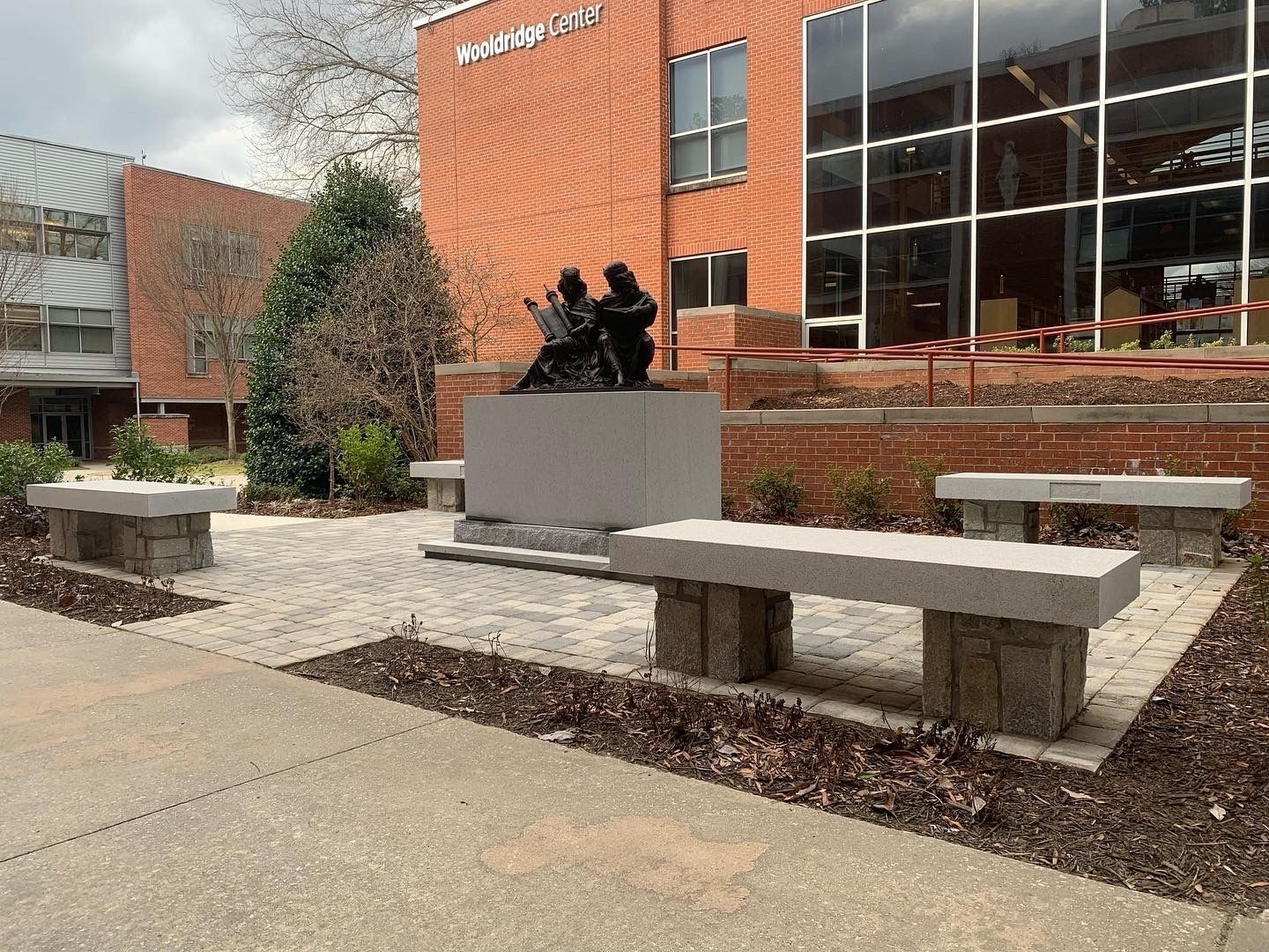 Outdoor plaza with benches and statue in front of a brick building.