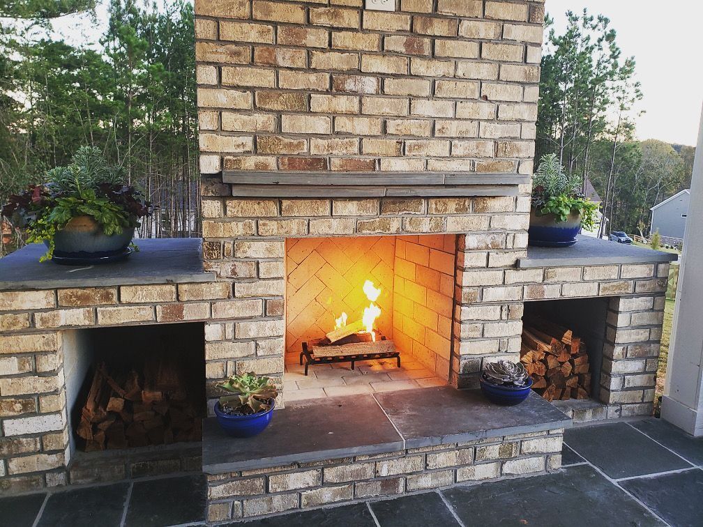 Outdoor brick fireplace with fire burning and firewood storage.