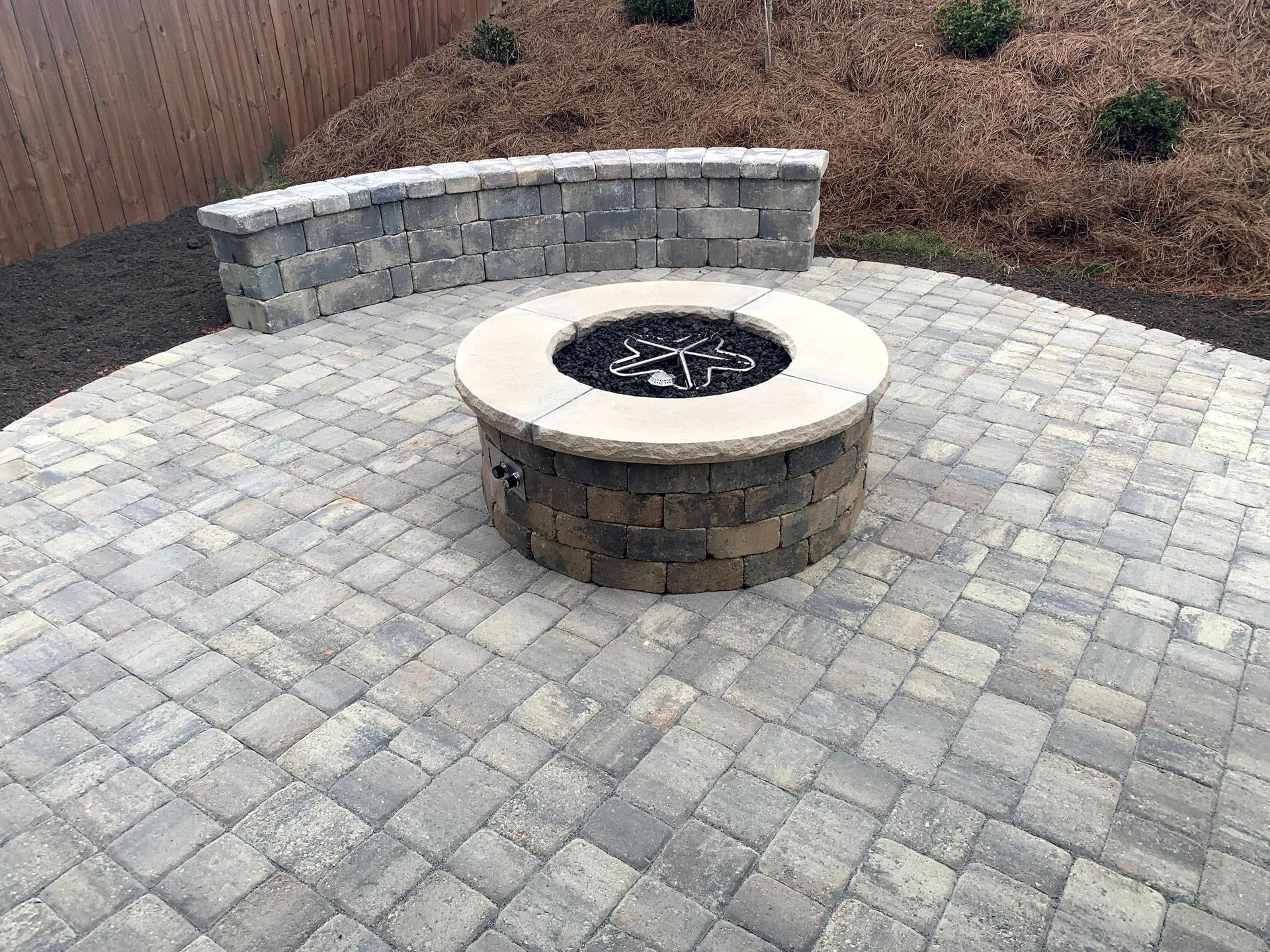 Fire pit on a stone patio with a low stone wall in a backyard setting.