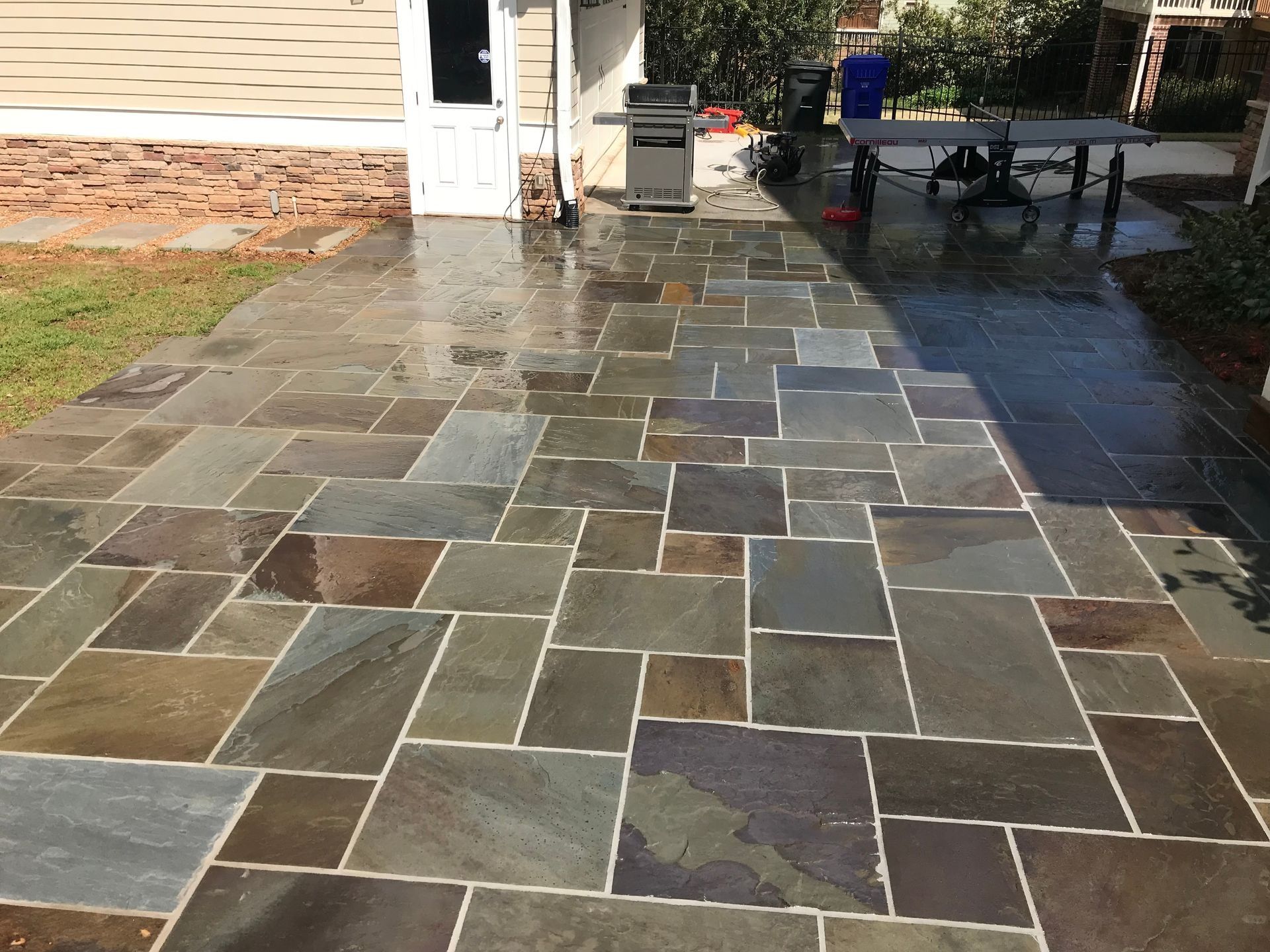 Patio paved with flagstone tiles, wet from recent rain. A grill and table sit nearby.