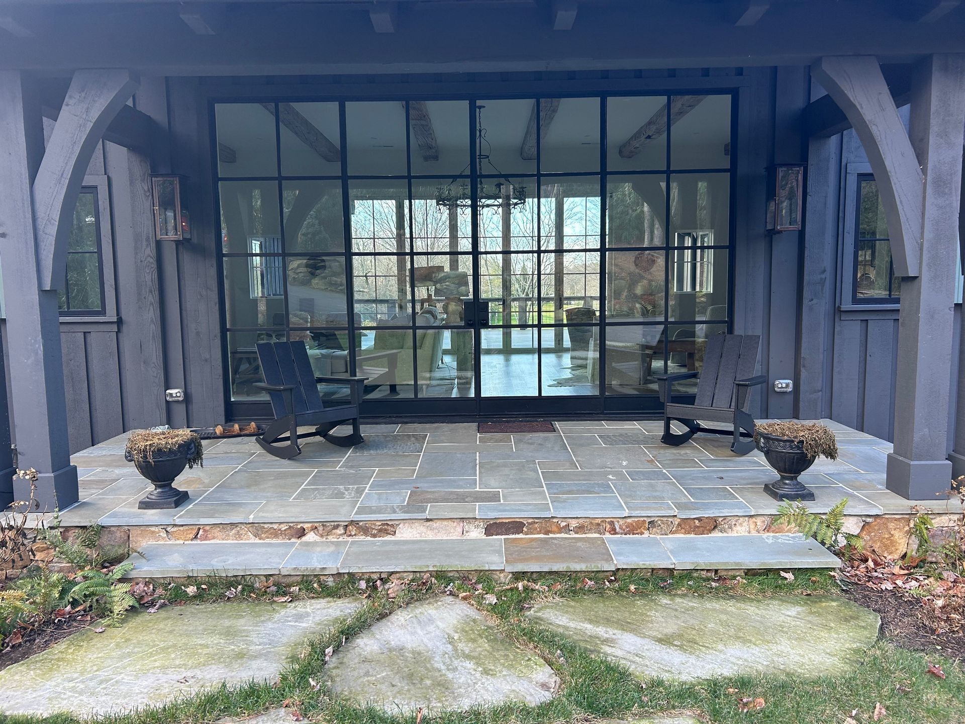 Front porch with glass door and black framing, flanked by rocking chairs and planters.