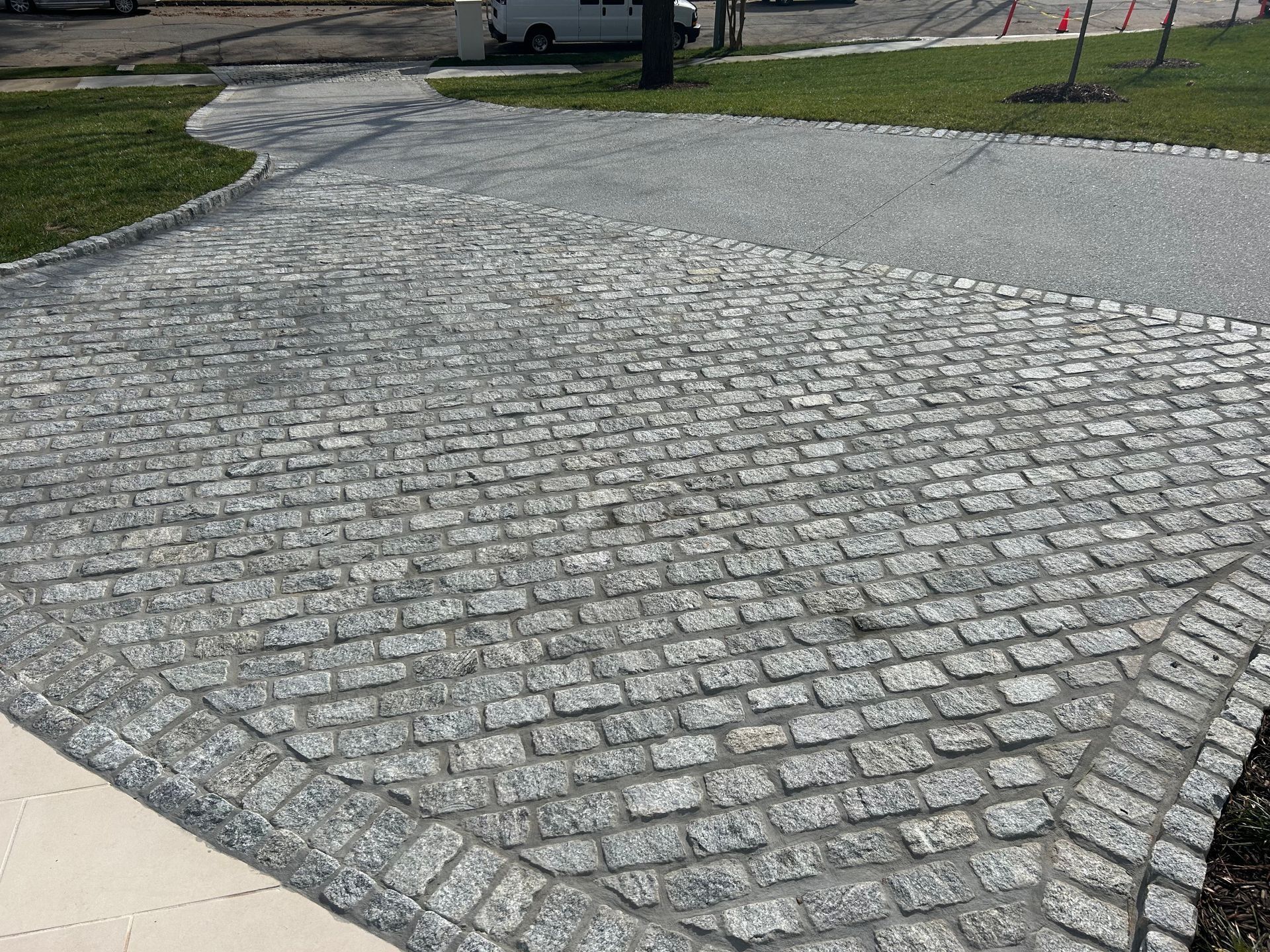 Cobblestone driveway and walkway with grassy edges and vehicle in the background.