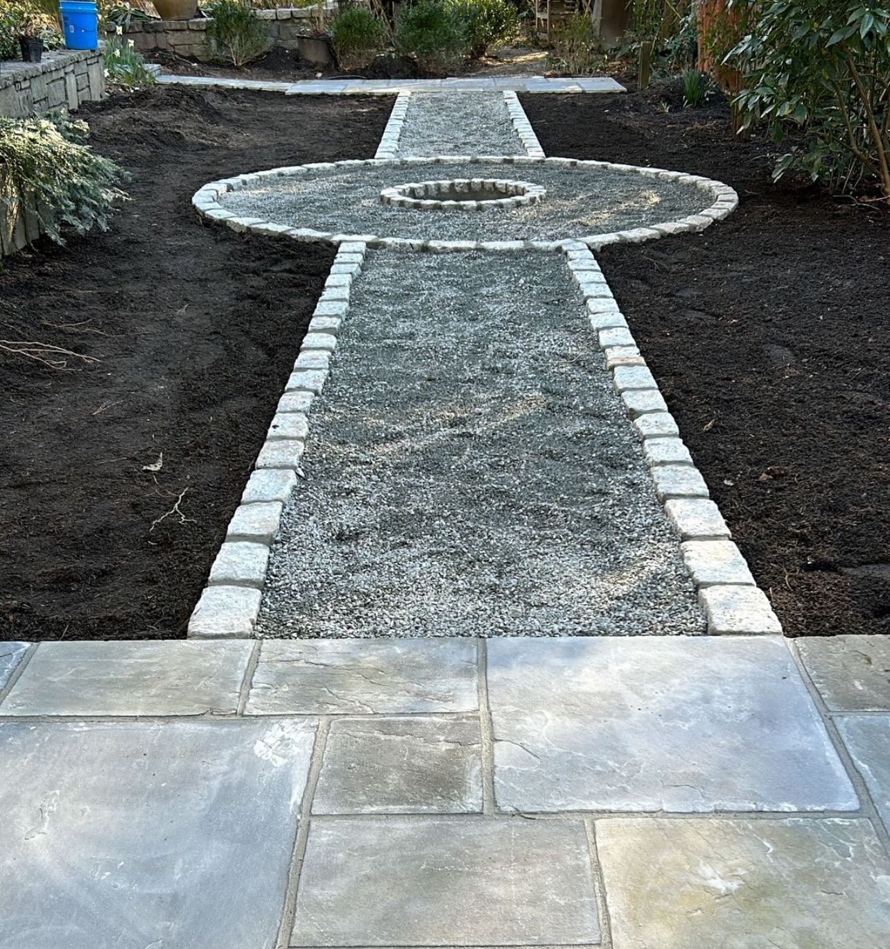 Garden pathway with stone pavers, gravel, and a central circular feature.