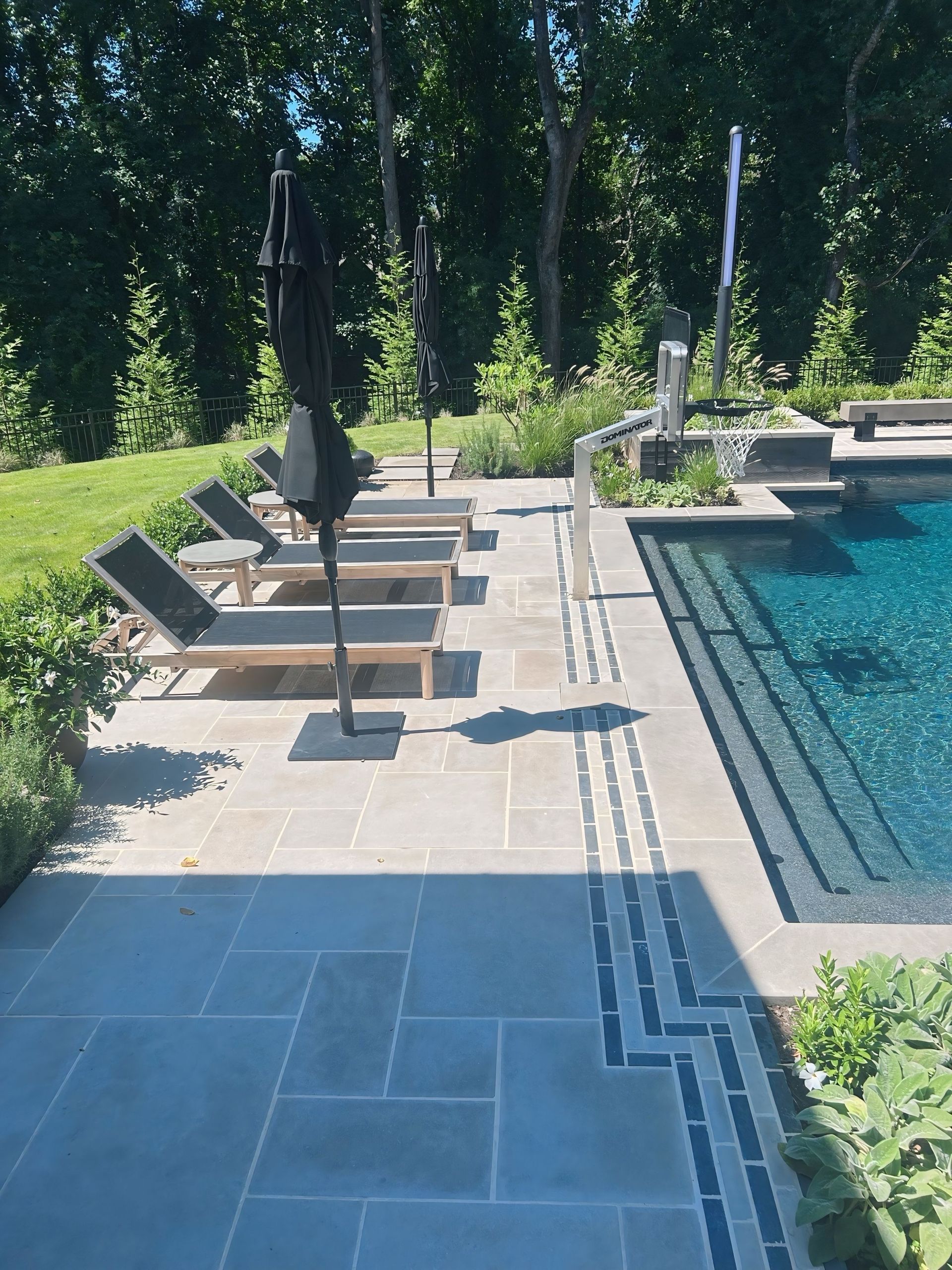 Poolside patio with lounge chairs, umbrellas, and steps leading into a pool.