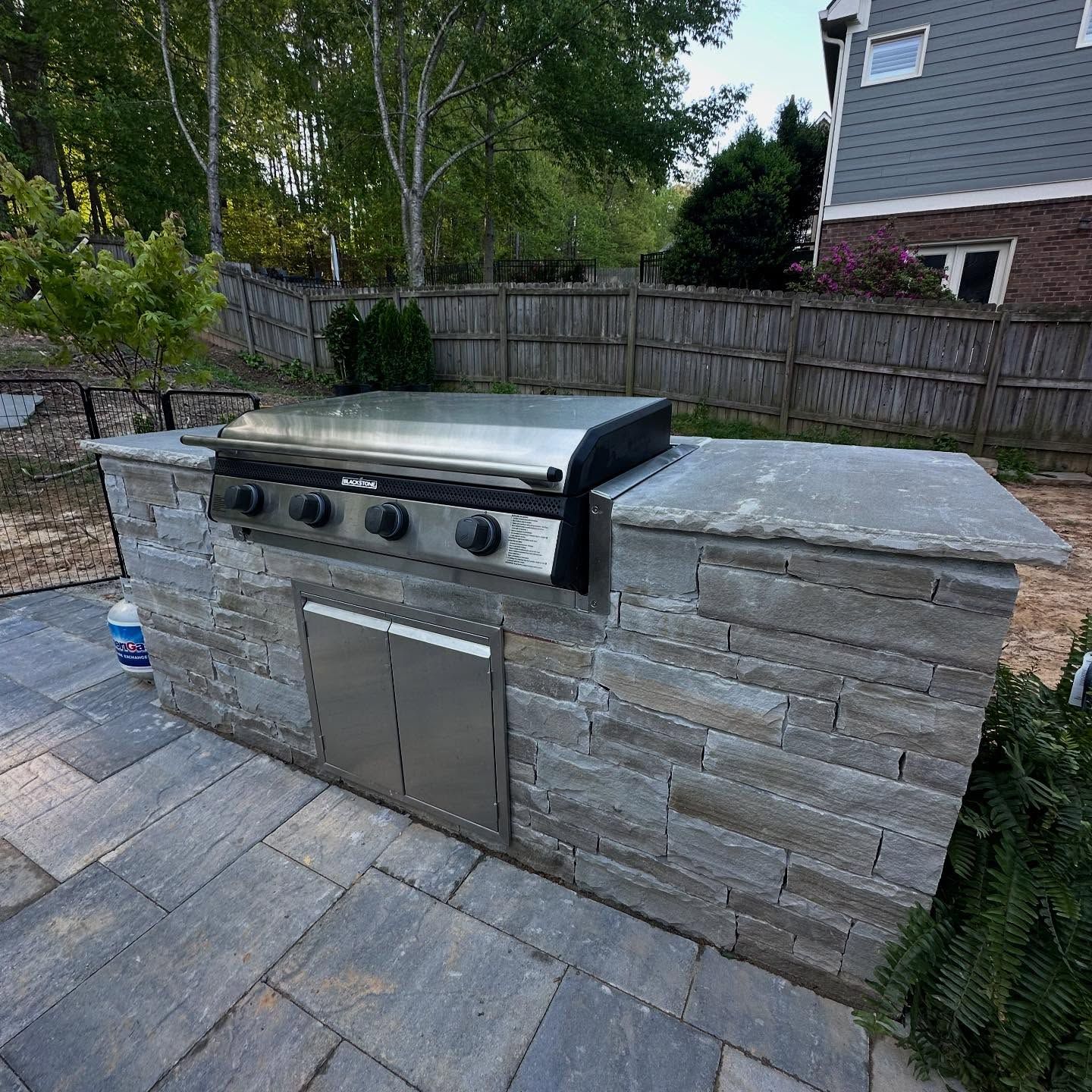 Outdoor kitchen with gray stone veneer and stainless steel grill and storage doors.