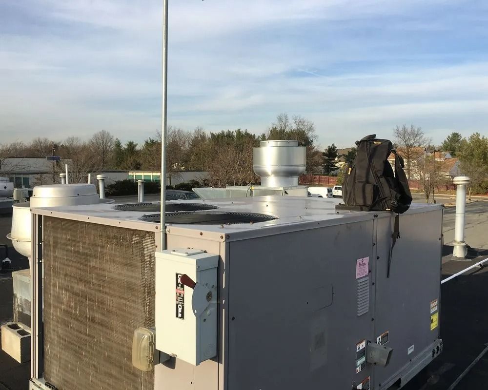 HVAC unit on a rooftop with a backpack on top. Blue sky and trees in the background.