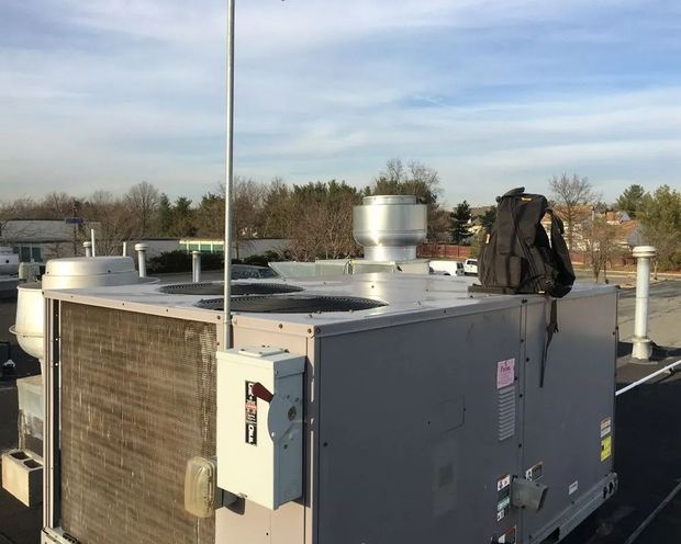 HVAC unit on a rooftop, with a backpack on top. Blue sky and trees in the background.