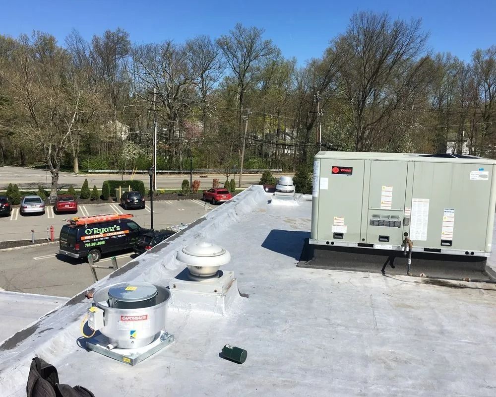 Rooftop scene with HVAC units, vents, and a service truck in a parking lot on a sunny day.