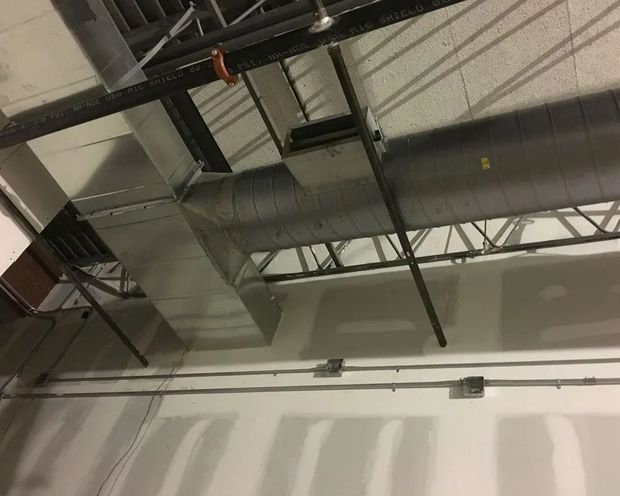 HVAC ductwork and electrical conduit installed on a ceiling with metal framing, adjacent to a drywall wall.