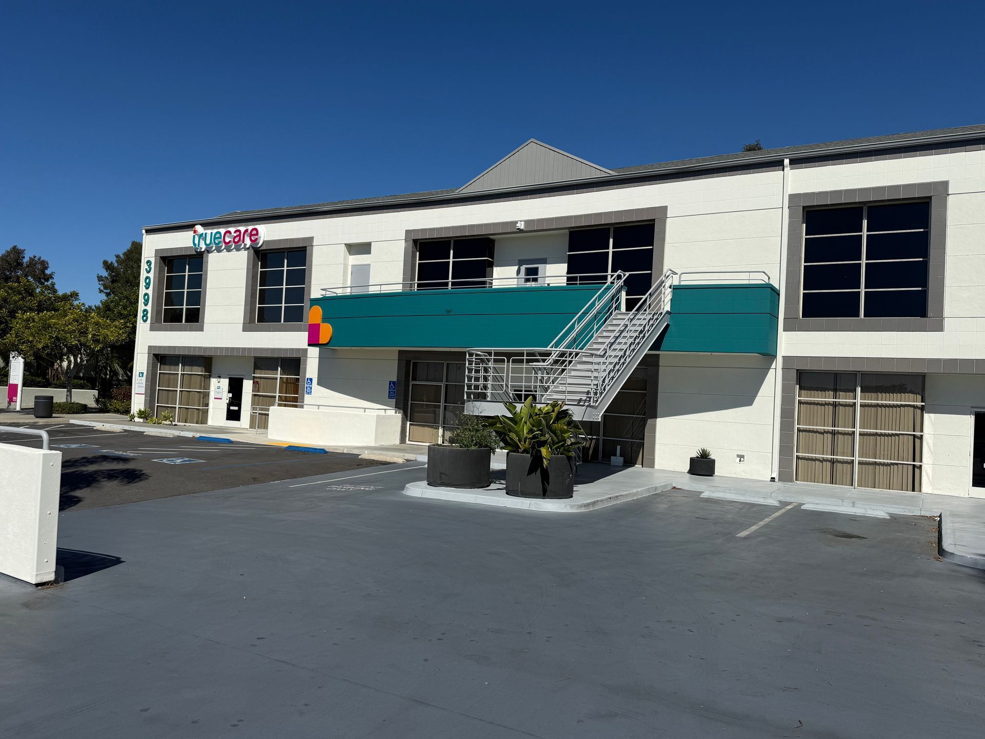 White building with teal awning, exterior staircase, and large windows on a sunny day.