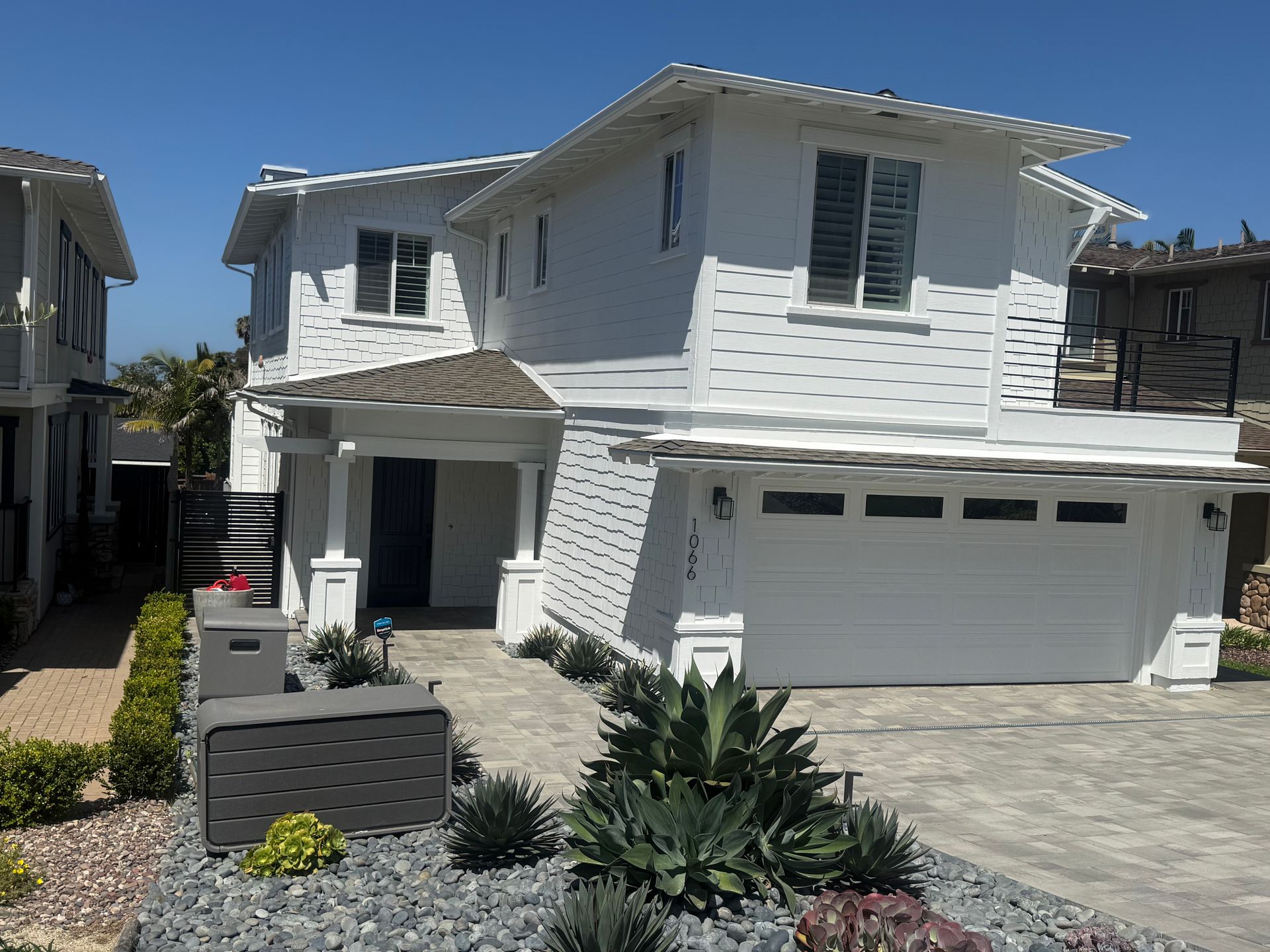White two-story suburban house with a gray garage, front entry, and desert landscaping under a clear blue sky