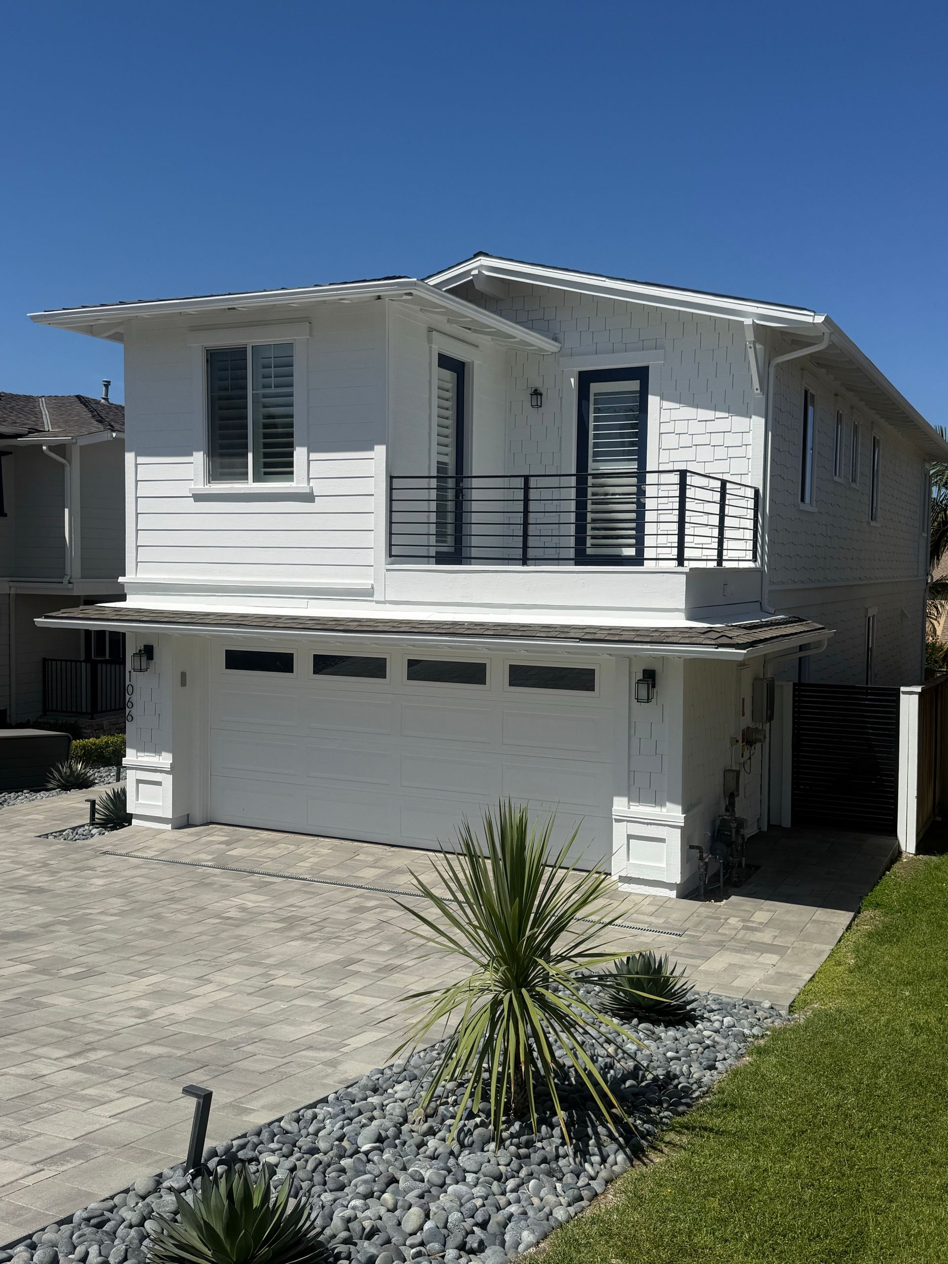 Two-story white house with balcony and garage under a clear blue sky