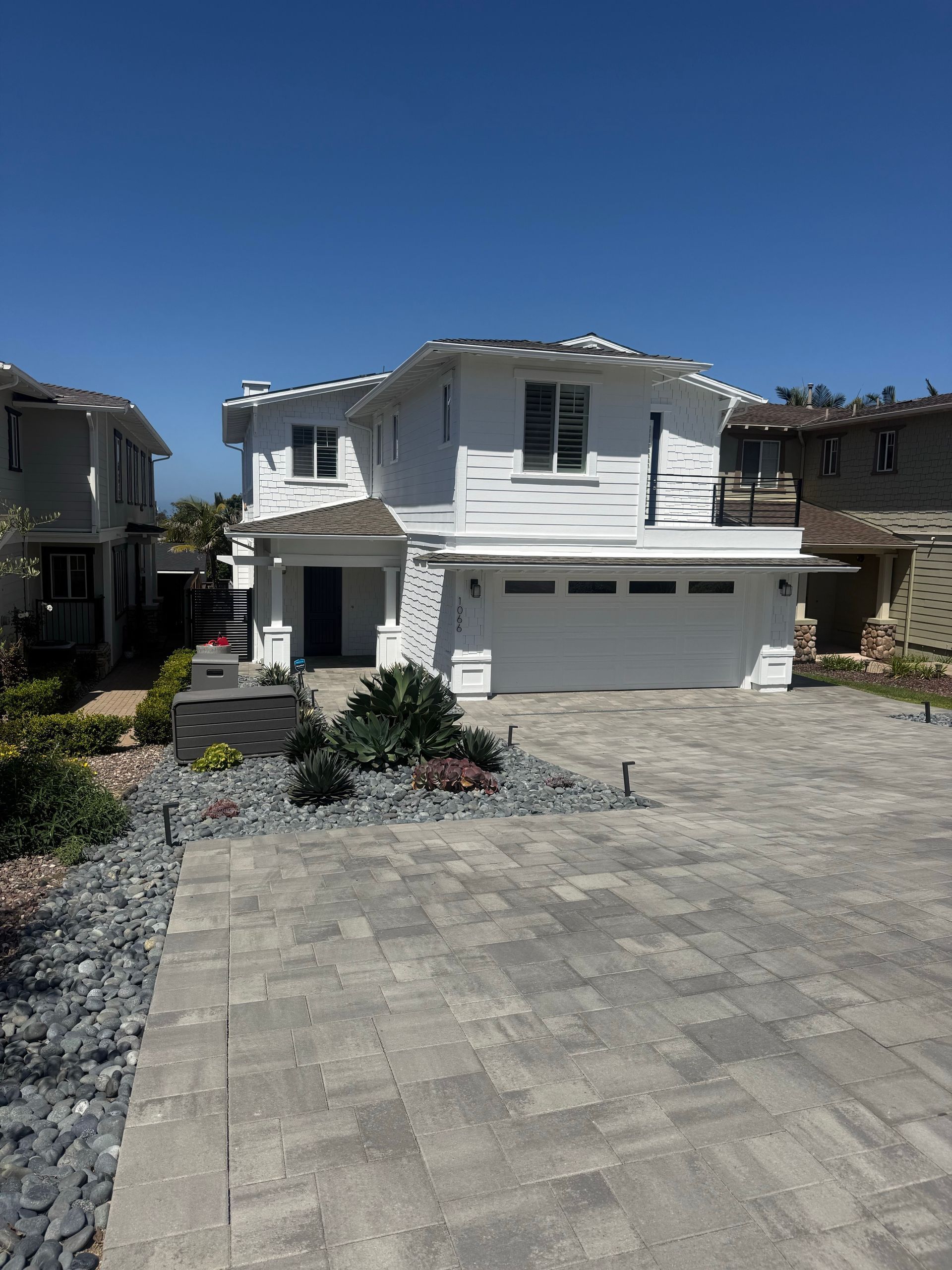 Two-story white suburban house with a driveway, garage, and desert landscaping under a clear blue sky